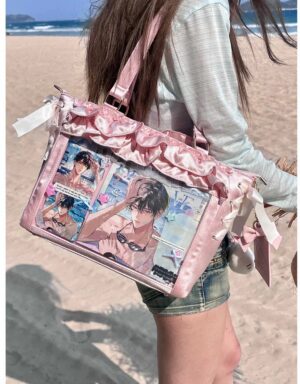 Pink satin Jirai Kei itabag with ruffled edges and anime badge display window, worn on shoulder at beach seaside location