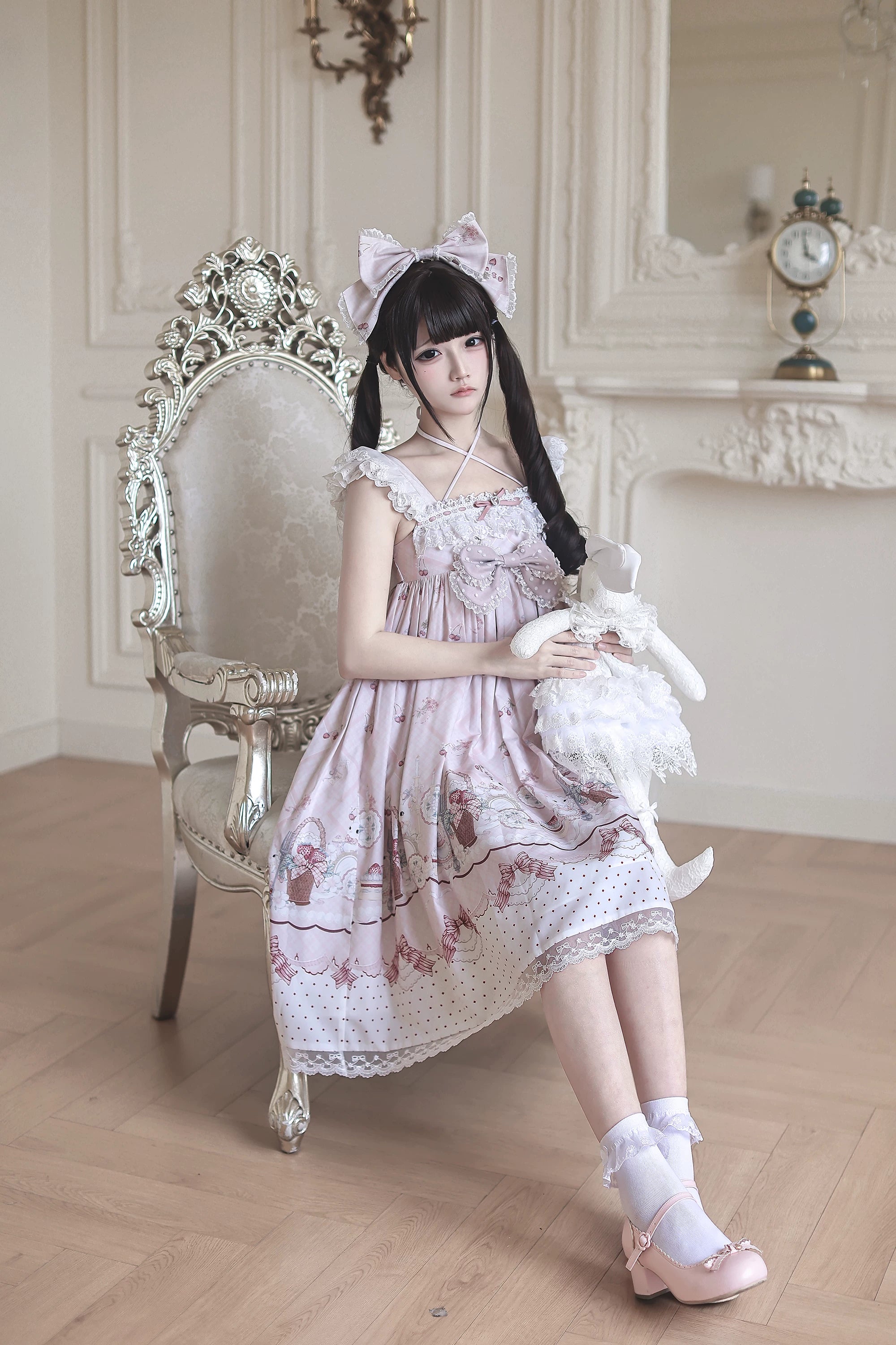 Sitting full-body shot of strawberry bunny Jirai Kei Lolita dress worn on carved chair model holding lace rabbit doll showing slip dress style and light pink heels