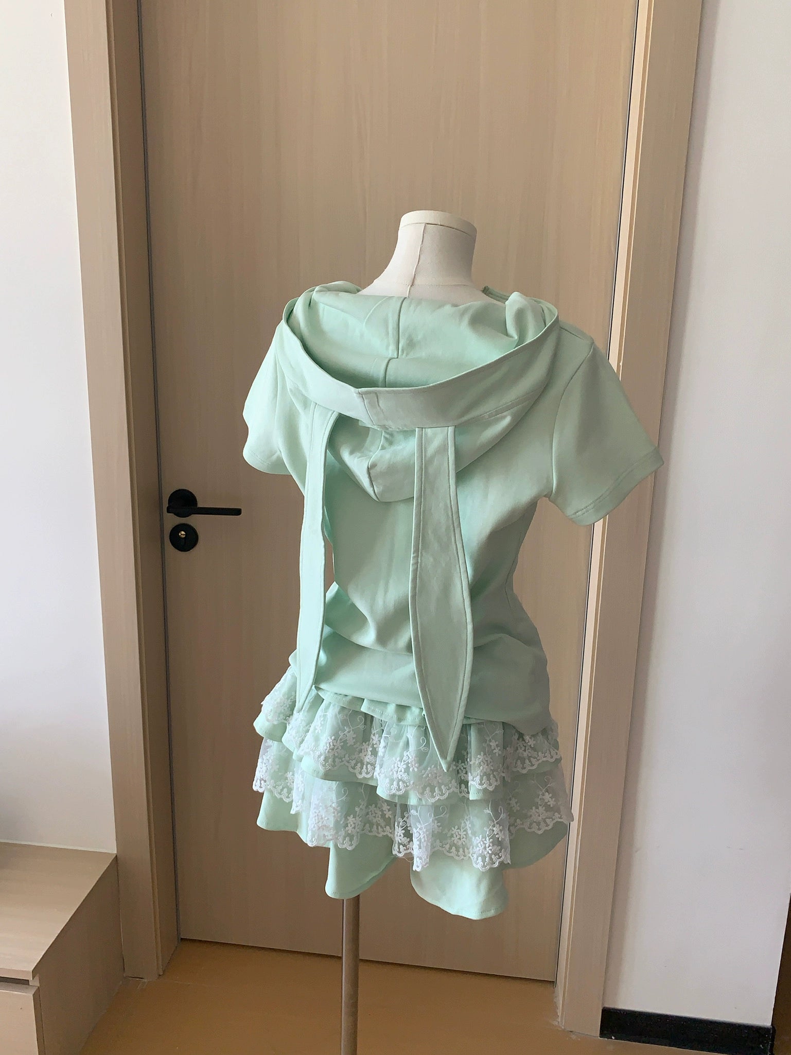 Back view of mint Jirai Kei bunny ear sweatshirt with lace ruffle skirt displayed on dress form mannequin, showing bunny ear hood design and layered lace hem details