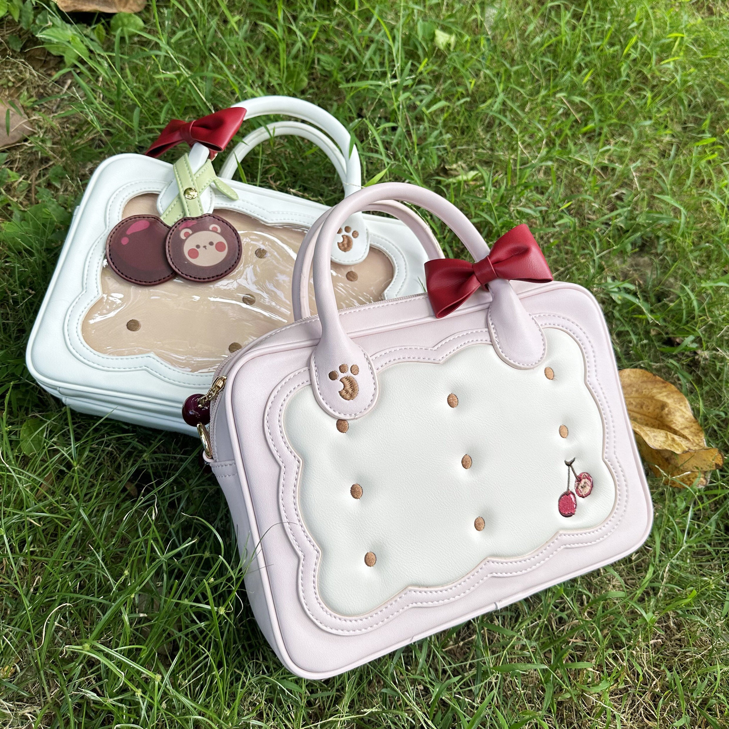 Two cherry bear cookie Jirai Kei crossbody bags in white and light pink with cherry embroidery side angle outdoor grass setting