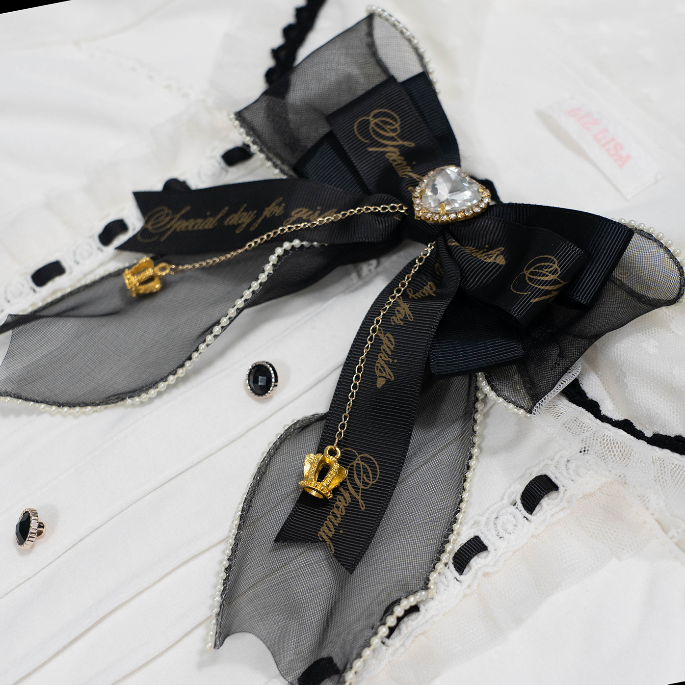 Black mesh and satin Jirai Kei bow brooch with gold lettering heart-shaped crystal hanging on vintage white shirt collar