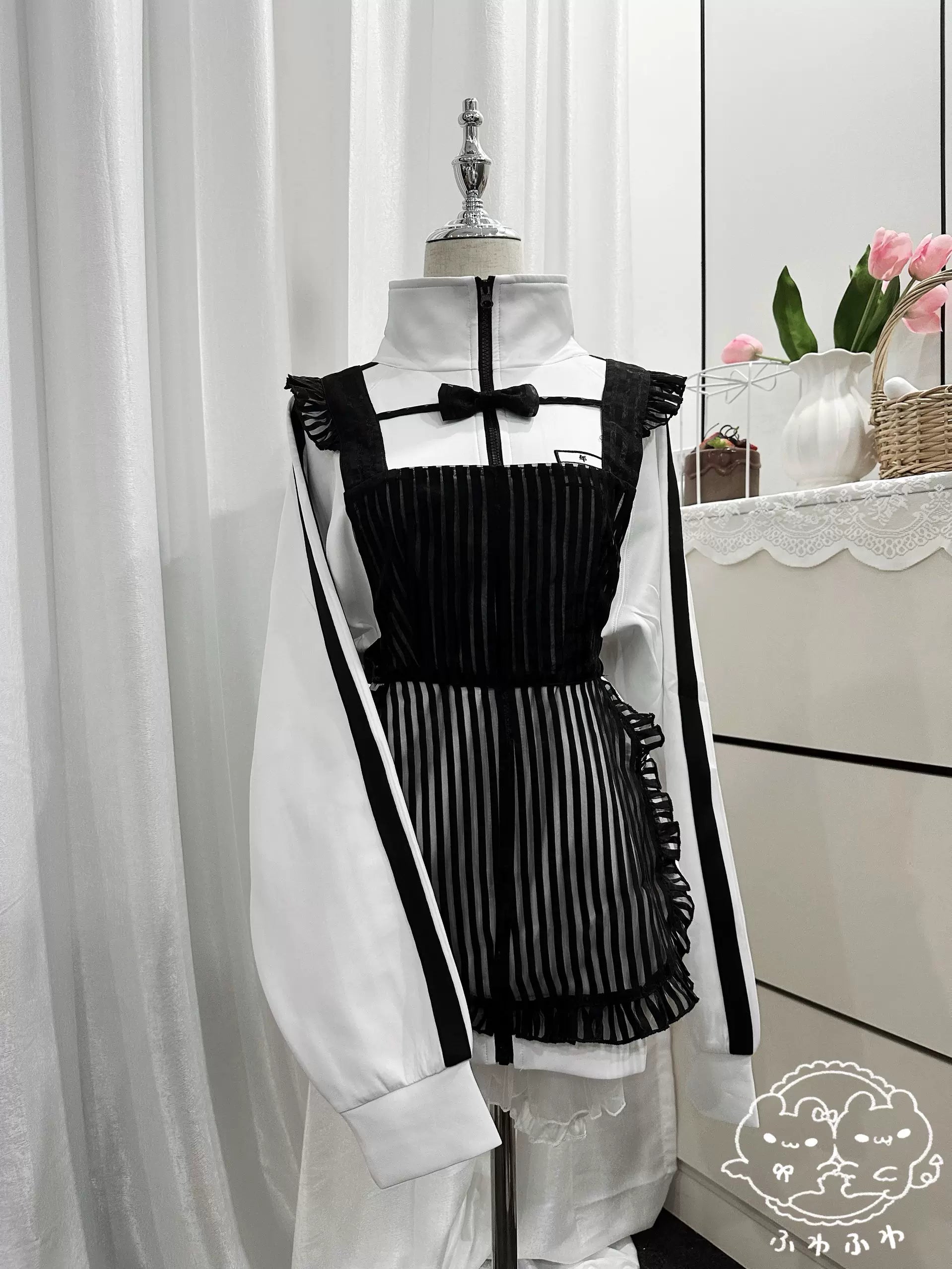 Black and white Jirai Kei sports jacket layered with pleated mesh camisole dress set, displaying fashion coordination with maid-style aesthetic, indoor home backdrop with floral decoration showing complete ensemble styling