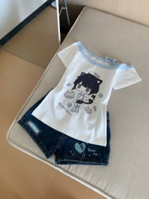 Off-shoulder Jirai Kei catgirl anime tee with light blue cold-shoulder trim and Japanese text, coordinated with blue denim shorts featuring heart prints, top-down flat photography