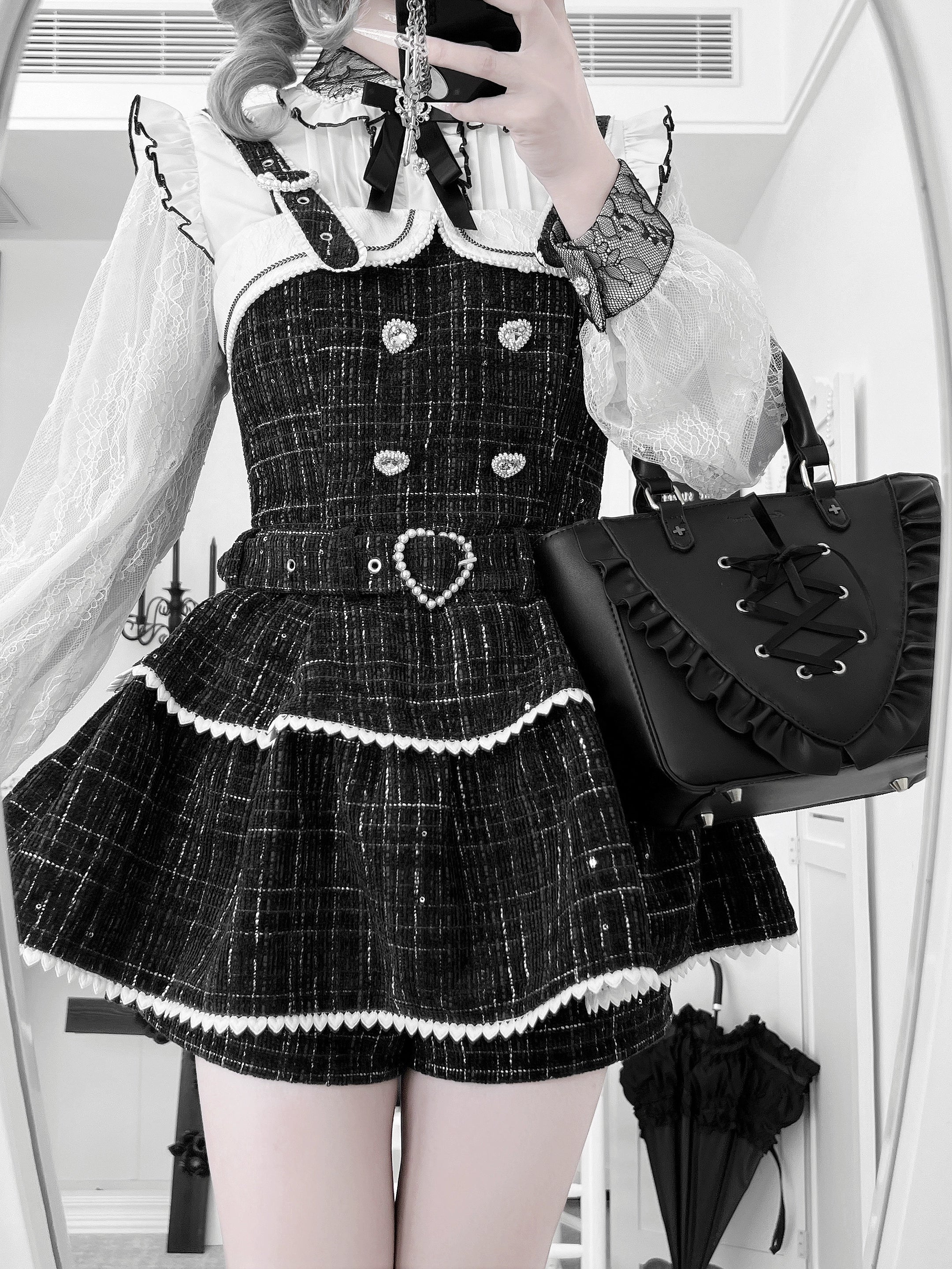Black plaid Jirai Kei suspender skirt close-up selfie showing heart-shaped buttons, ruffled details, and matching shorts