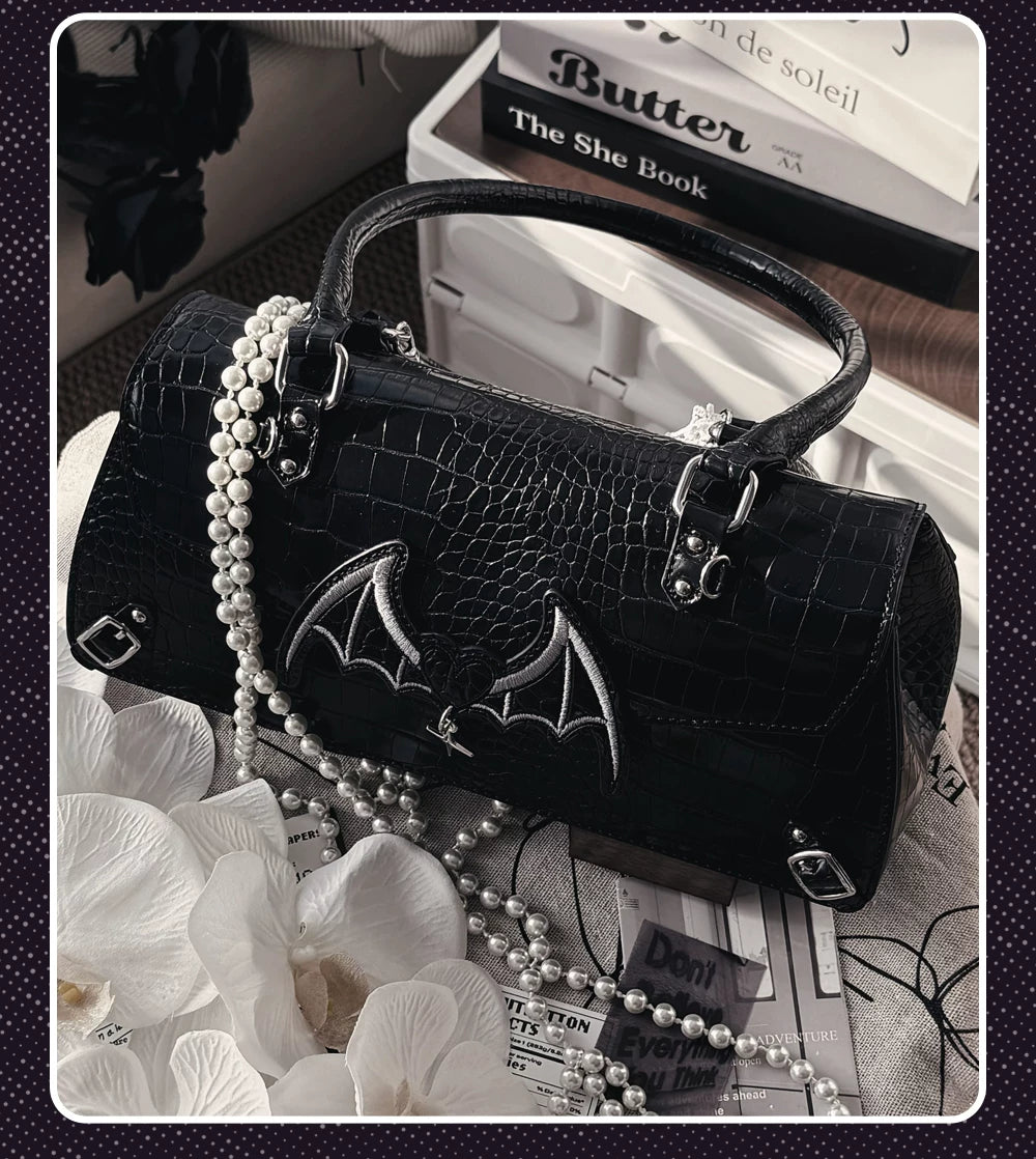 Black bat-style croc handbag with pearl chain strap and bat wing embroidery decorated with artificial flowers and books