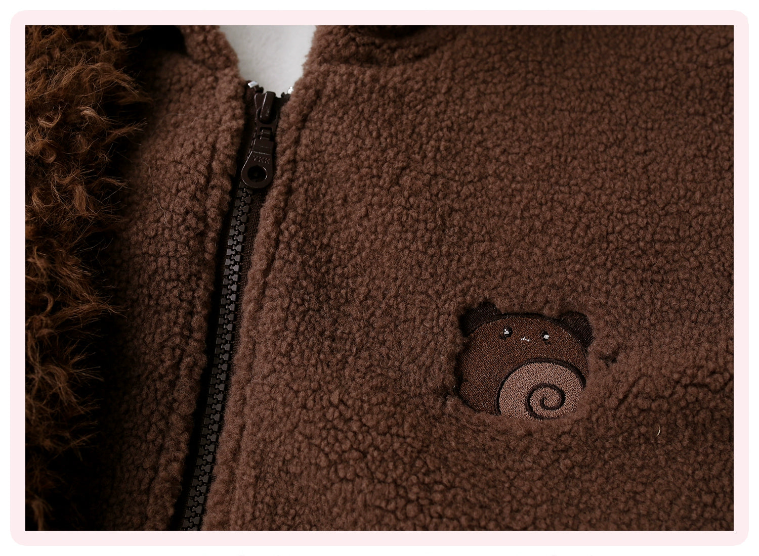 Close-up flat shot of brown bear face embroidery detail on fleece jacket showing fine embroidery work, visible metal zipper track, and professional craftsmanship quality