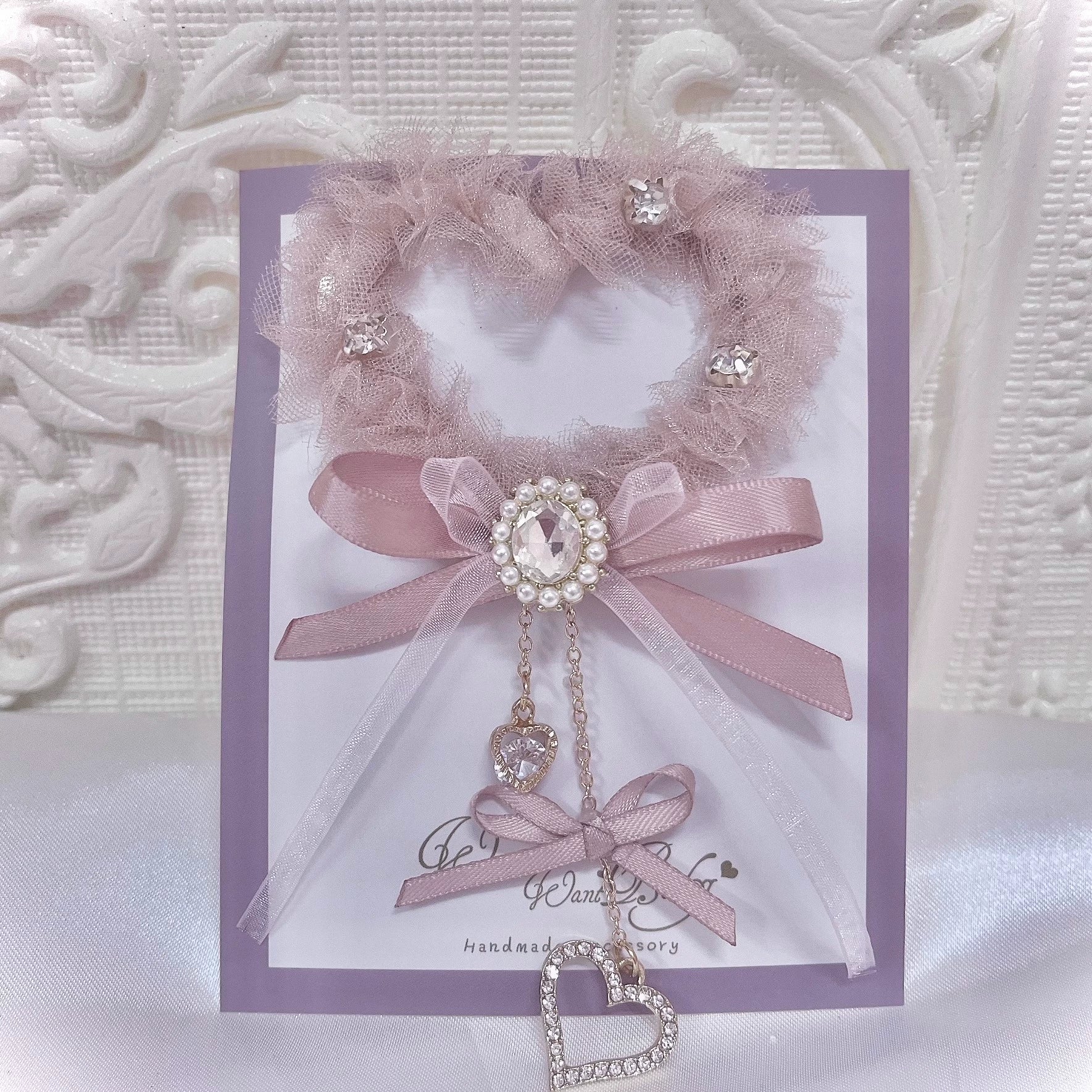 Pink heart-shaped tulle hair clip with rhinestones and satin bow featuring heart pendant charm, displayed on branded card