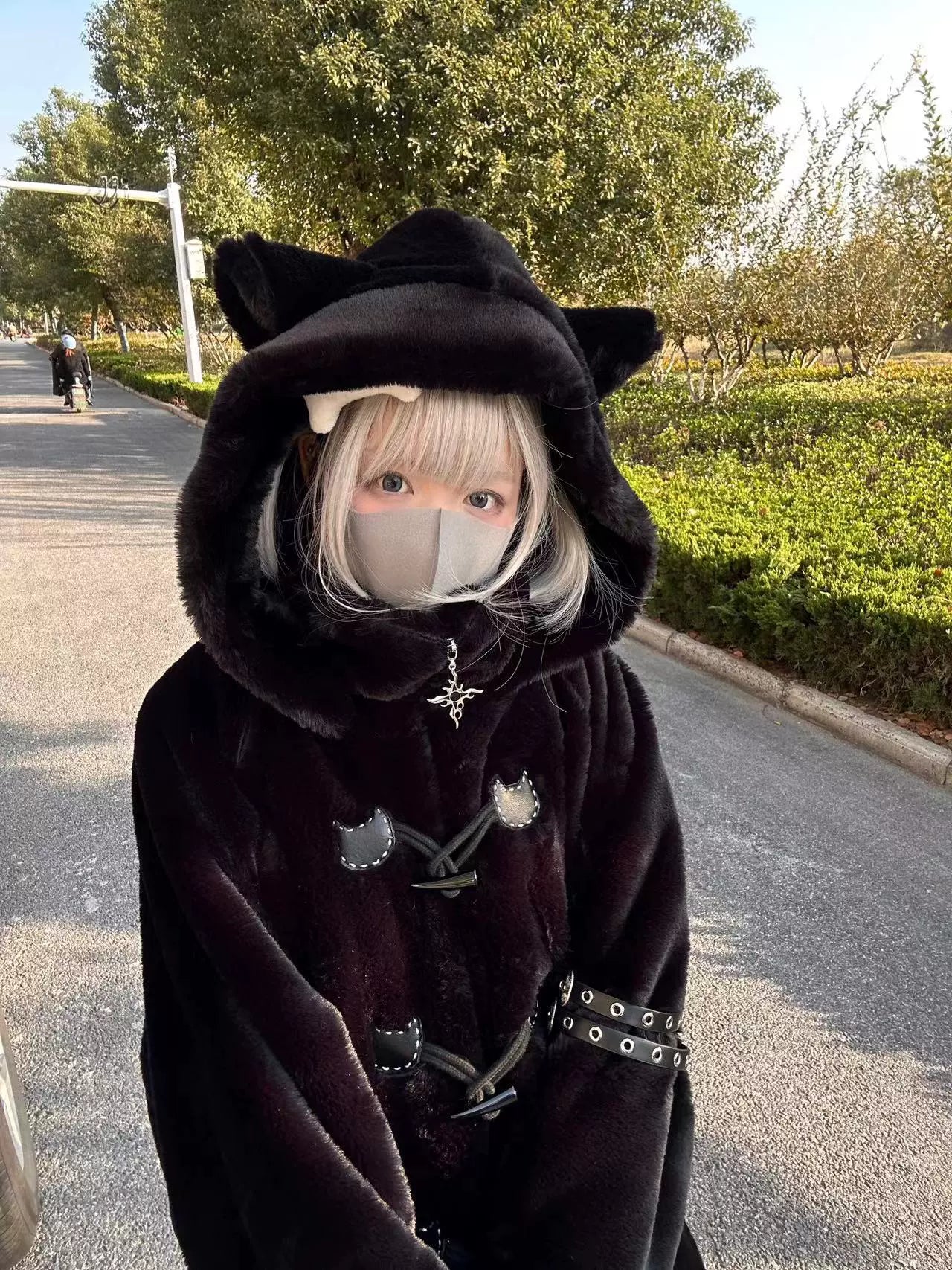Dark black fuzzy cat ear hooded coat half-front view blonde girl outdoor roadside face mask decorative horn toggles