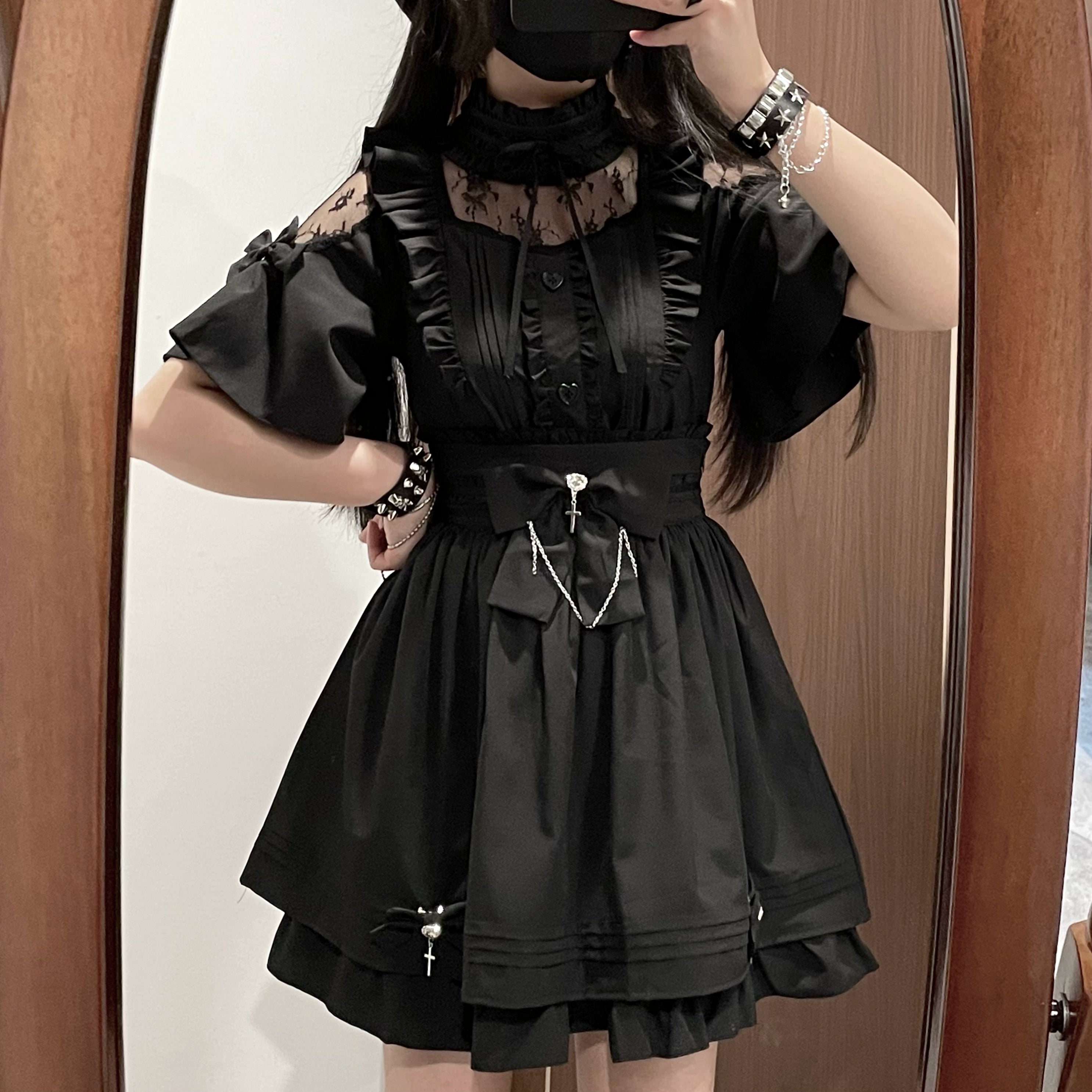 Half-body side mirror selfie of all-black jirai kei two-piece set with ruffled short sleeves, lace neck trim, detachable bow with cross chain, layered ruffled skirt hem
