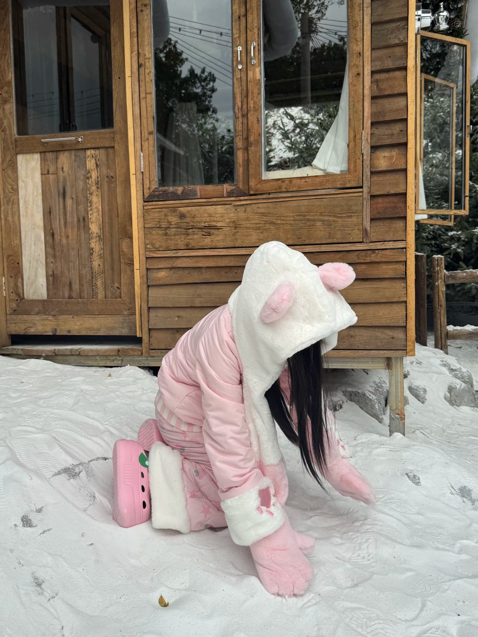 Pink Jirai Kei winter padded coat with bear ear hood, fleece-lined fuzzy collar, matching gloves, and strawberry patch pants, low front side angle kneeling pose