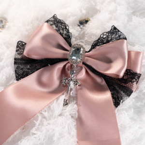 Pink satin Jirai Kei bow hair clip brooch with black lace edge square crystal center and decorative cross pendant charm close-up