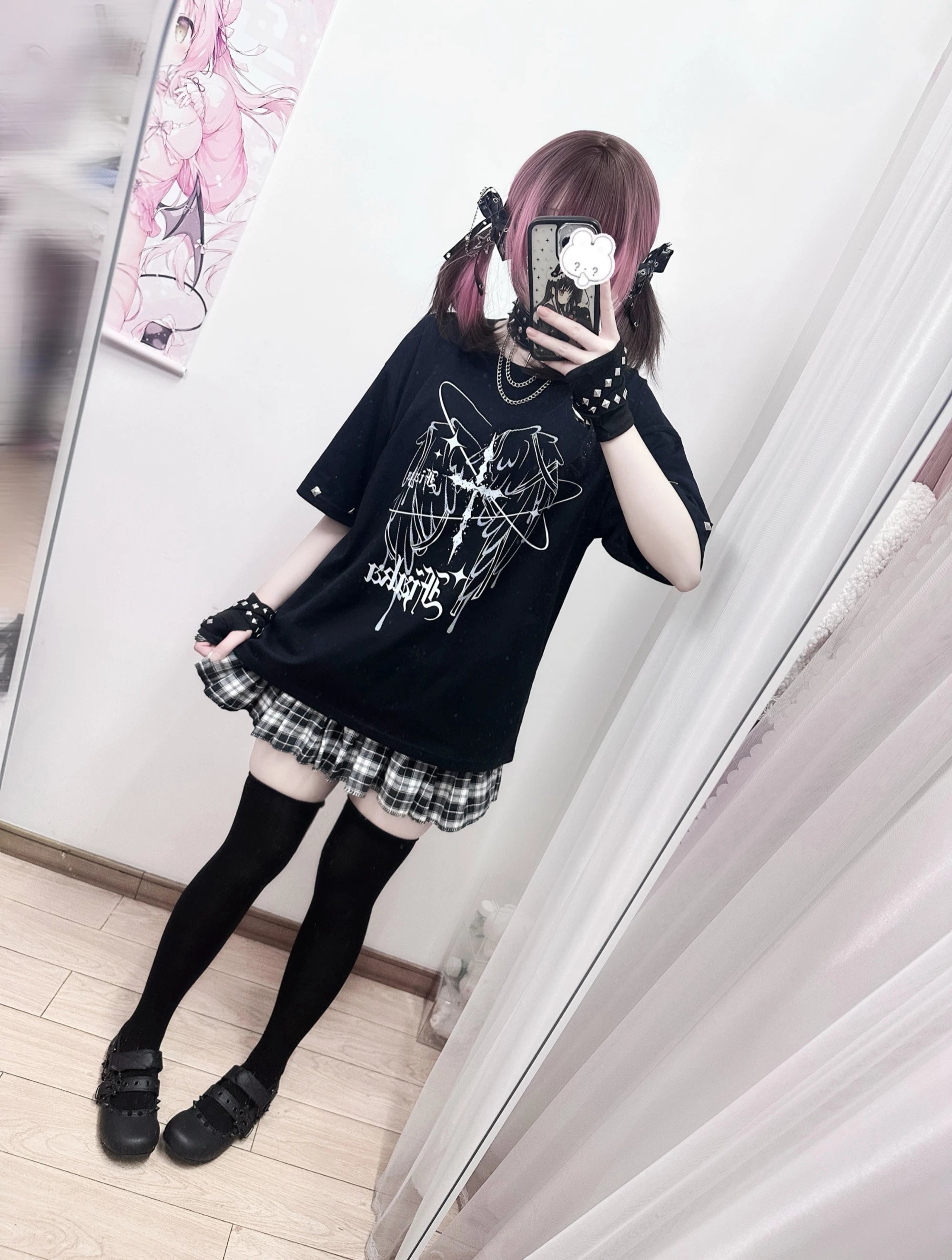 Side profile mirror selfie of Jirai Kei oversized black graphic t-shirt, female model wearing matching plaid skirt set with cartoon phone case and studded accessories