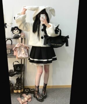 White fluffy rabbit-ear jirai kei hooded jacket with pink button closures and cross bow sleeve details worn by model in black pleated skirt and platform boots, full-body rear mirror selfie perspective