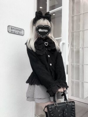 Black Ryousangata Jirai Kei coat with faux fur collar and ruffled cuffs, three-quarter front view on model at outdoor doorway entrance