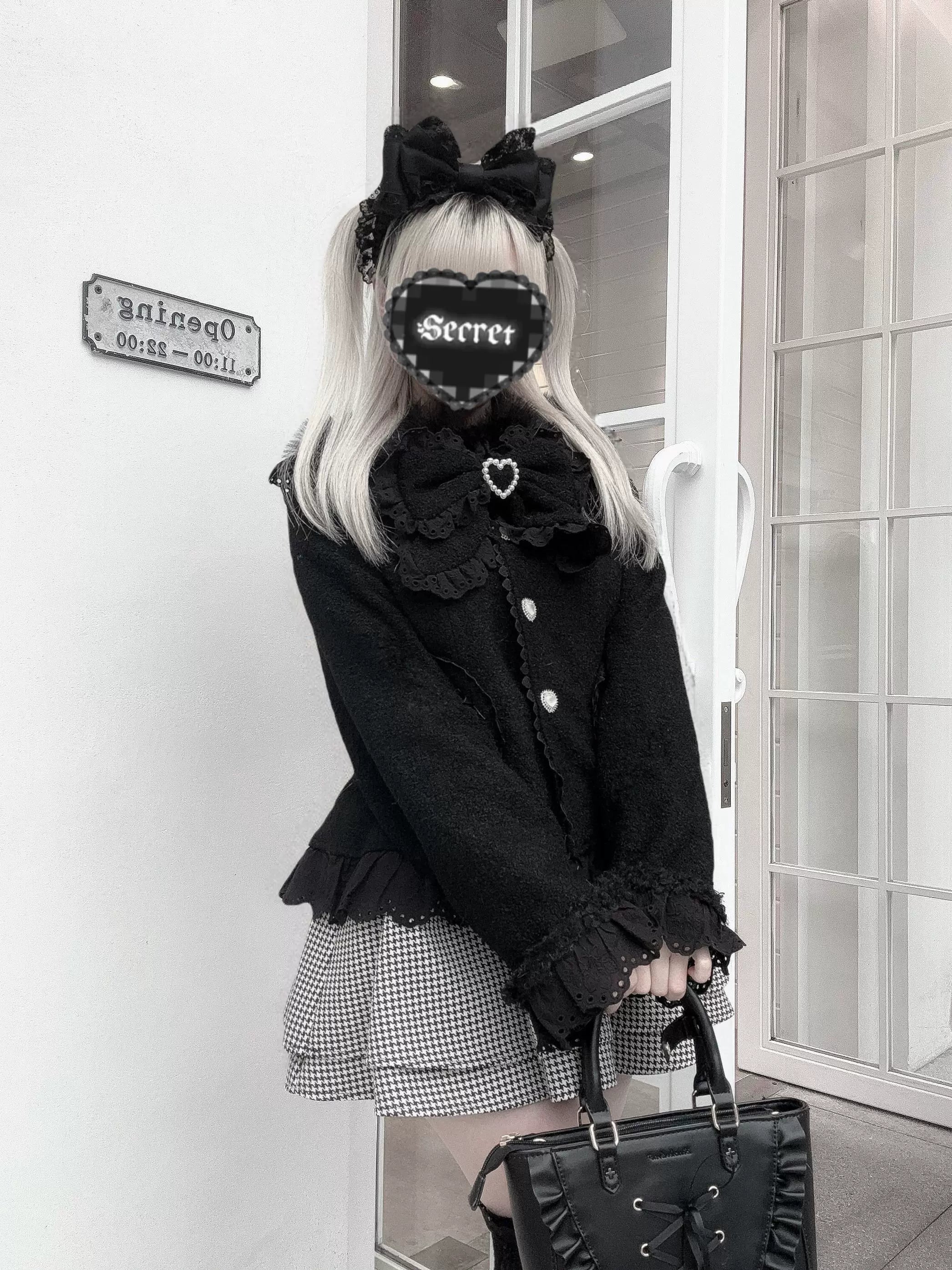 Black Ryousangata Jirai Kei coat with faux fur collar and ruffled cuffs, three-quarter front view on model at outdoor doorway entrance