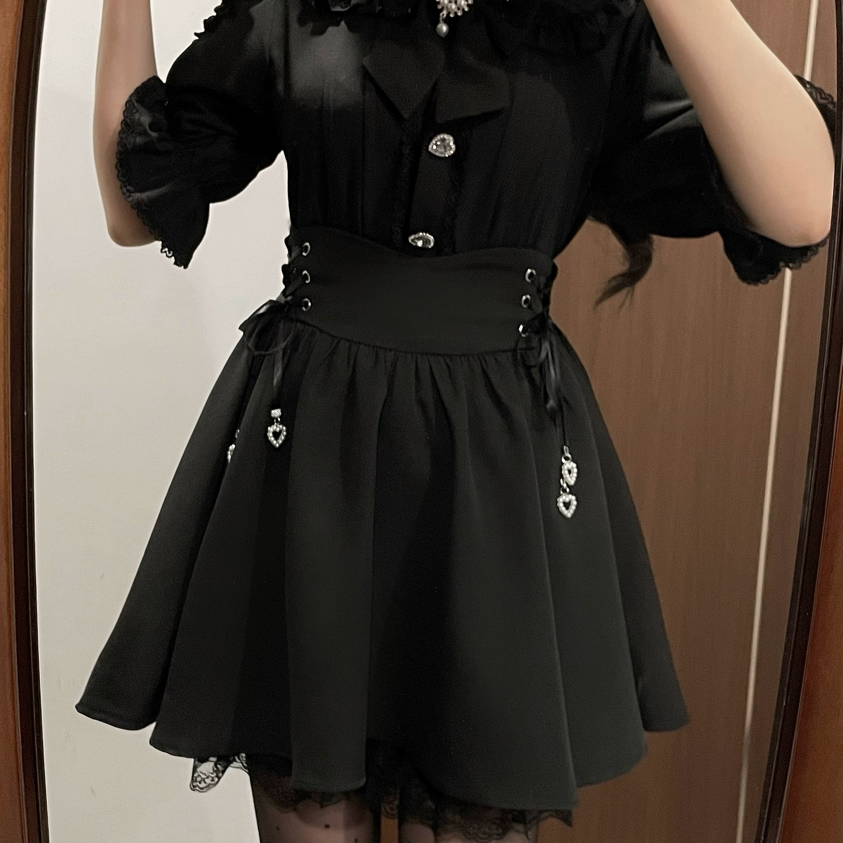Black Jirai Kei skirt and blouse set medium shot mirror selfie detail view, showcasing A-line lace-trimmed skirt hem, corset waist construction, hanging heart pendant charms, and puffed sleeve design - jirai kei fashion details