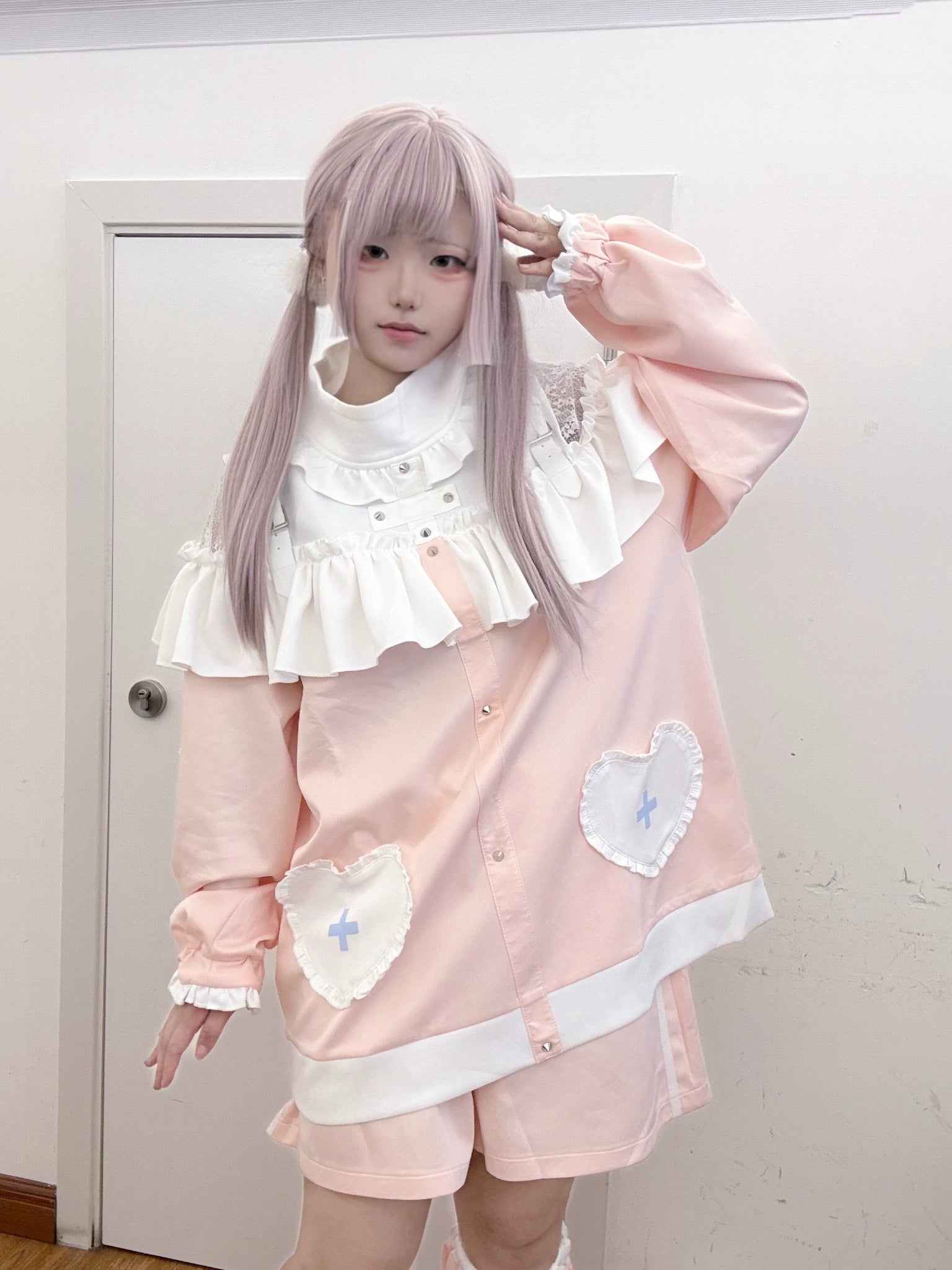 Pink sweatshirt and matching shorts three-quarter front shot with ruffled collar and heart-cross pockets, hand touching hair pose