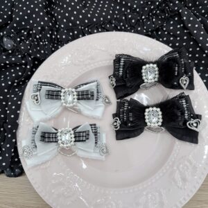 Jirai Kei bow hair clips overhead flat lay showing black and white houndstooth pattern variant with lace trim and rhinestone heart charms on embossed white plate