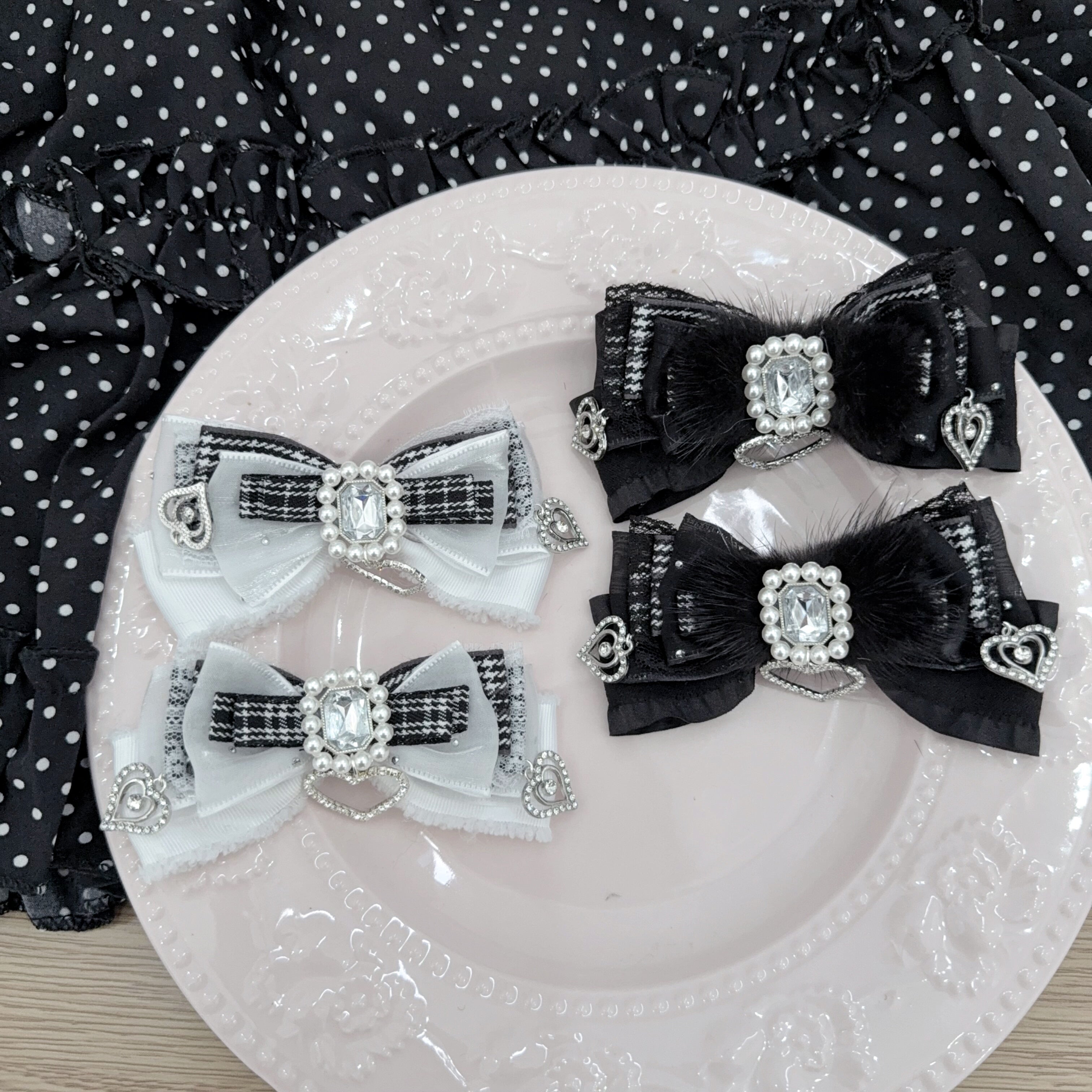 Jirai Kei bow hair clips overhead flat lay showing black and white houndstooth pattern variant with lace trim and rhinestone heart charms on embossed white plate