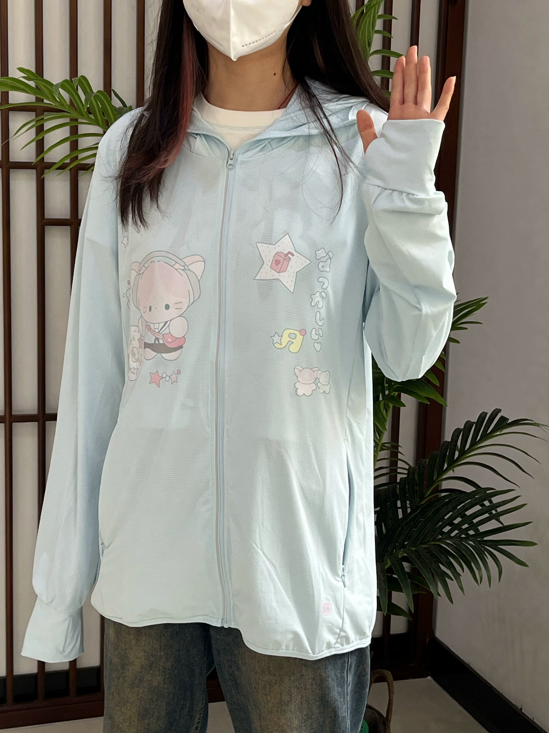 Jirai kei style sun protection jacket on dark-haired model in indoor space with potted plants, showcasing full zip-up construction and cartoon print details