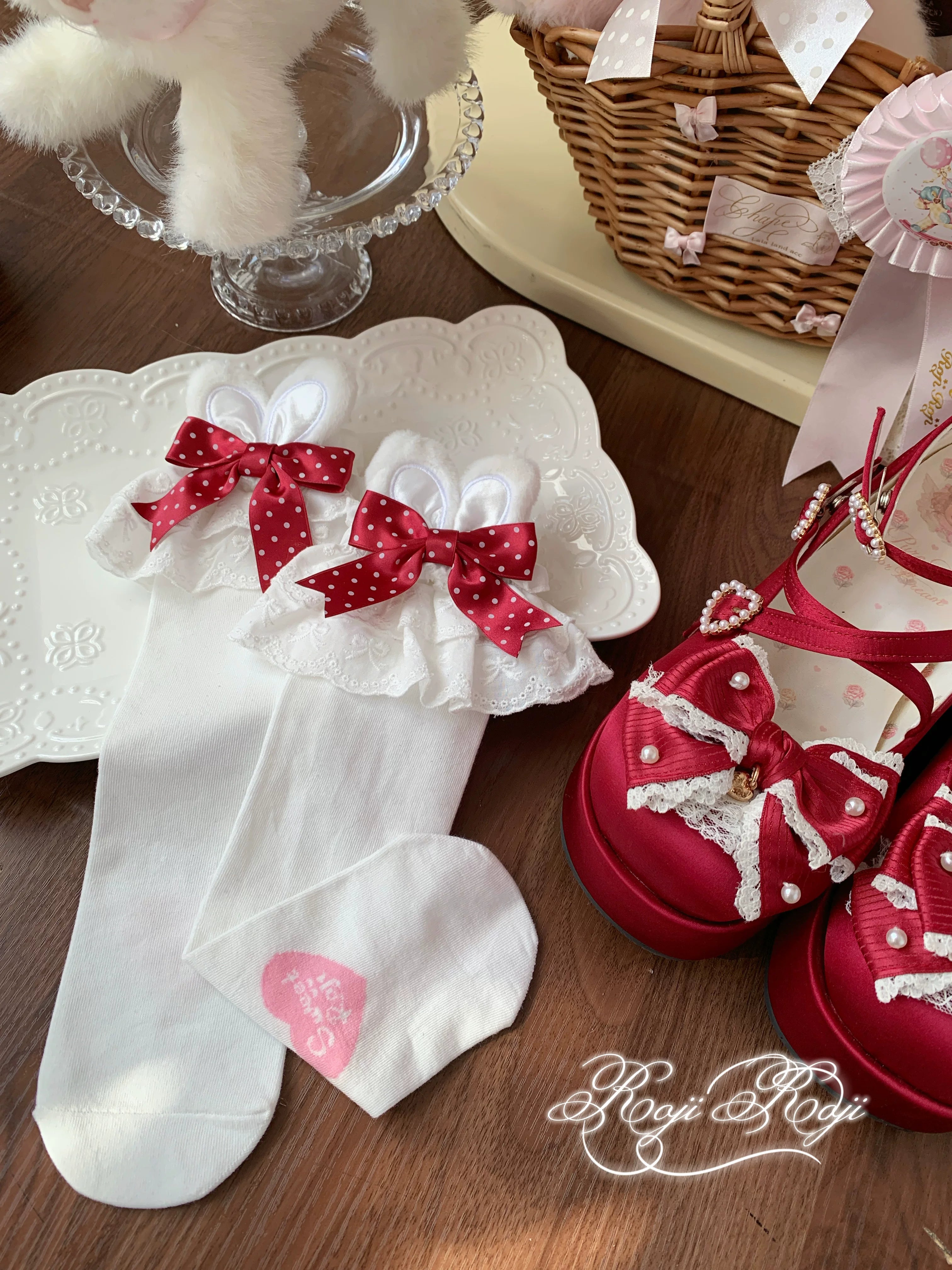 Close-up top-down view of Jirai Kei red polka dot bunny ear socks held by hand with white base and delicate lace trim with plush toys