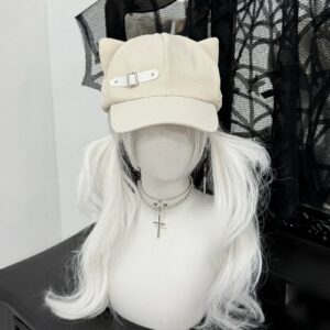 Ivory beige cat ear beret cap with suede-like texture and leather strap buckle, front flat lay view, gothic dark backdrop, alternative fashion peaked cap