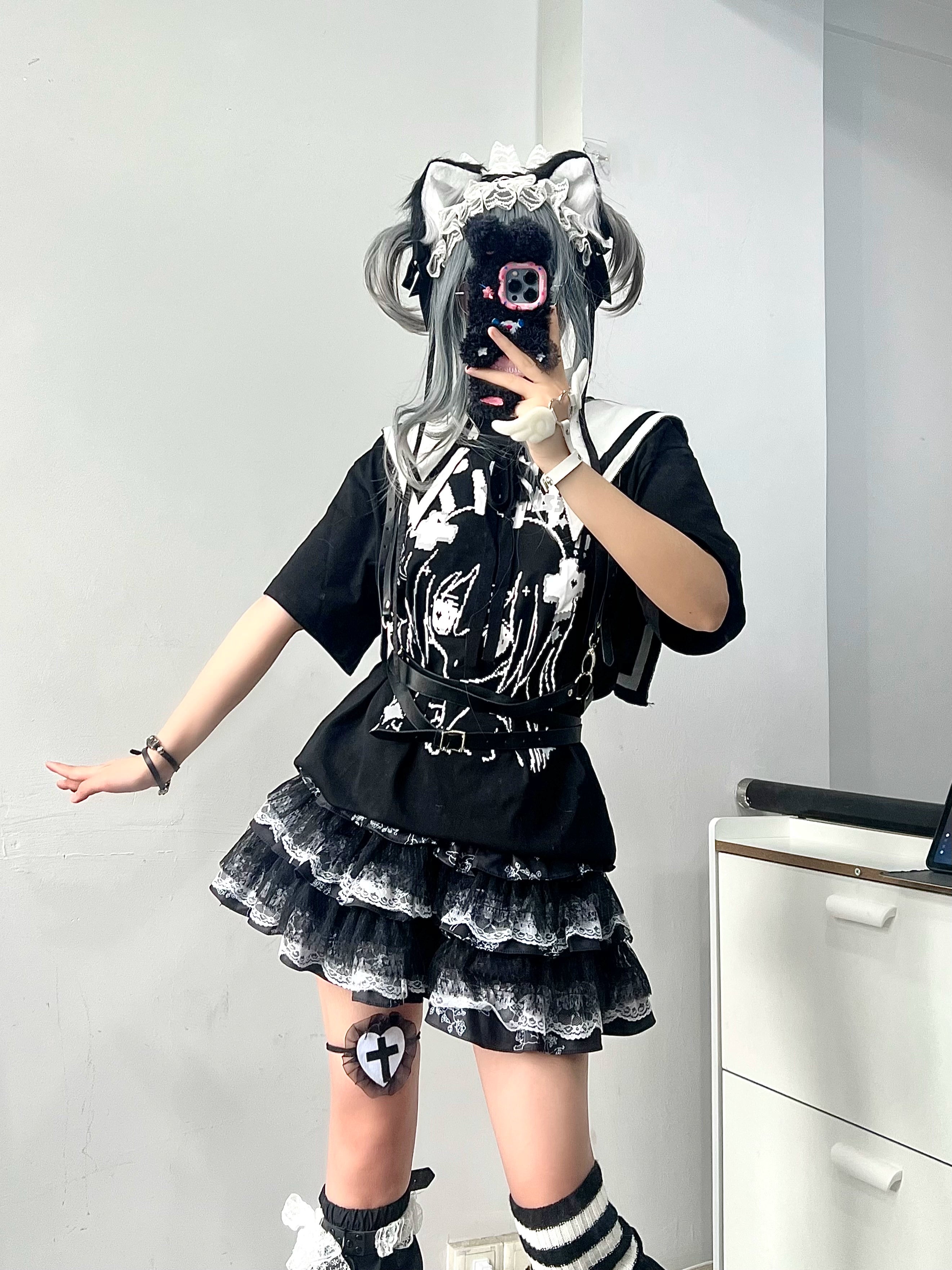 Jirai Kei girl wearing layered lace puff skirt with cat ear twin bun headdress and printed black top mirror selfie three-quarter angle view