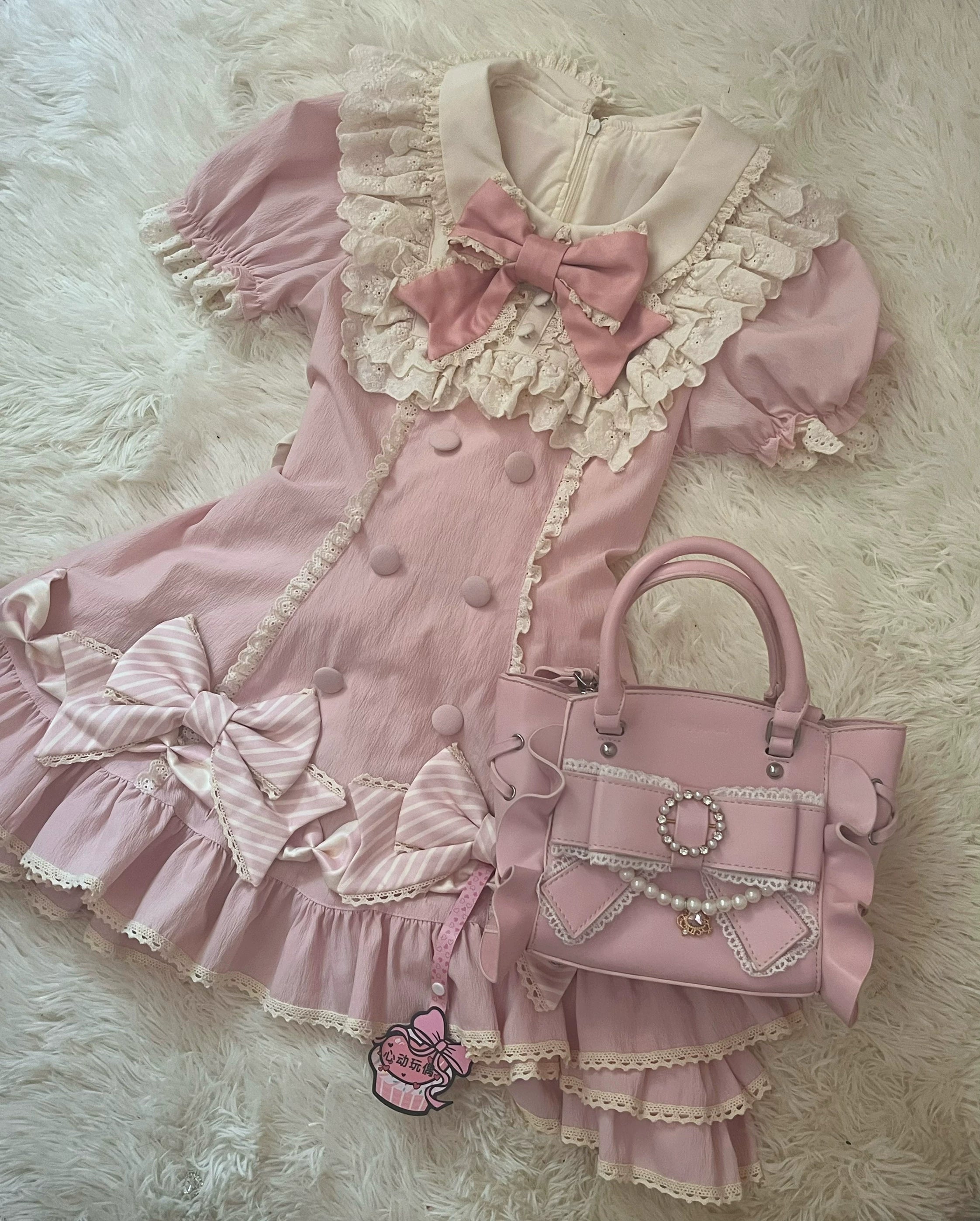 Pink Jirai Kei handbag paired with matching pink lolita dress overhead flat lay featuring lace collar, puffed sleeves, ruffled hem, decorative bows, and cupcake bag charm on white fluffy carpet