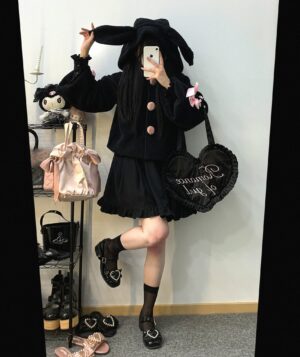 Black plush rabbit-ear jirai kei hooded jacket with round front buttons and pink floral sleeve trim cross bow decorations, modeled in black pleated skirt with heart-shaped handbag mirror selfie