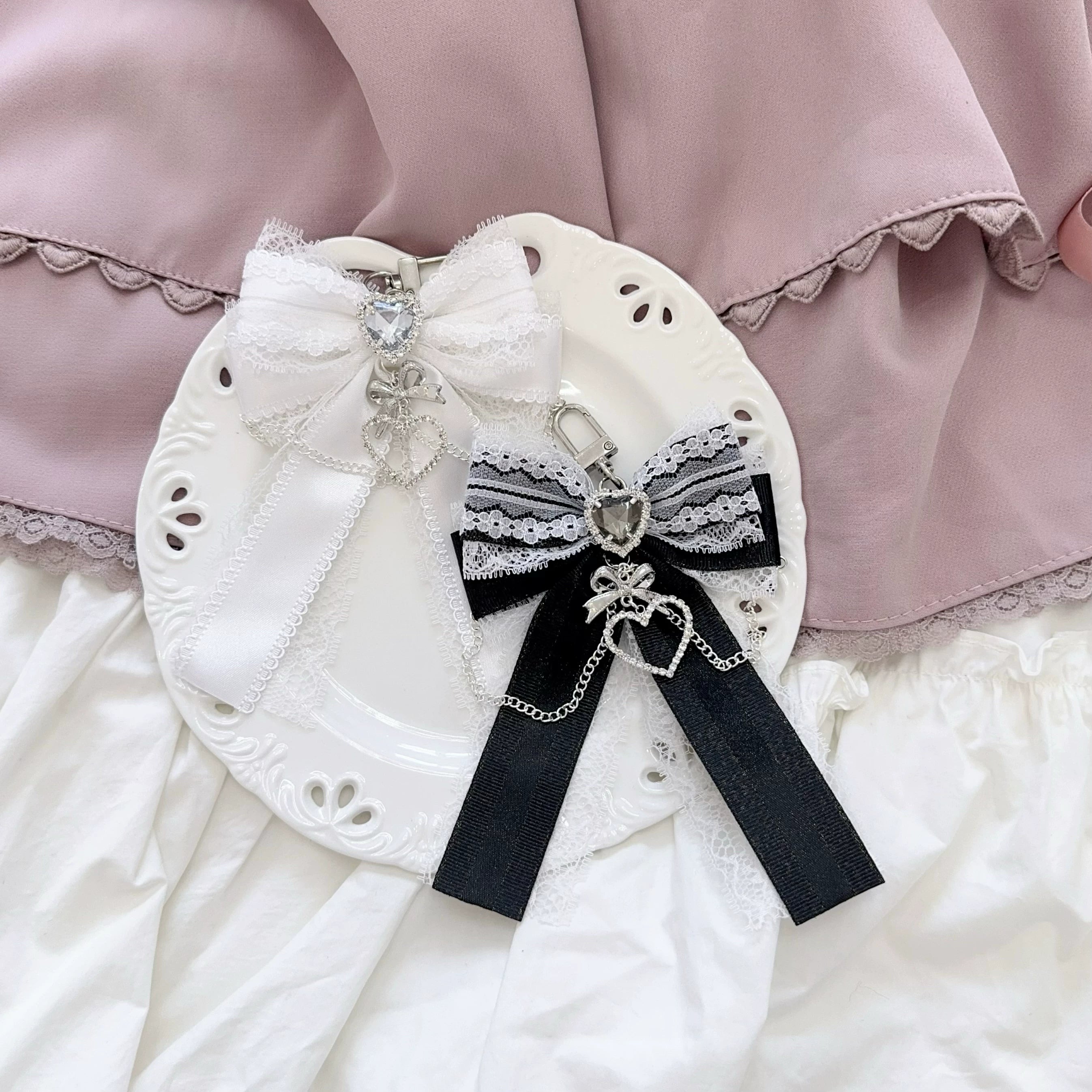 Black-white and multicolor mismatched Ryousangata bow bag pendants overhead flat lay with lace decorative plate - heart rhinestone and chain charm details for aesthetic styling