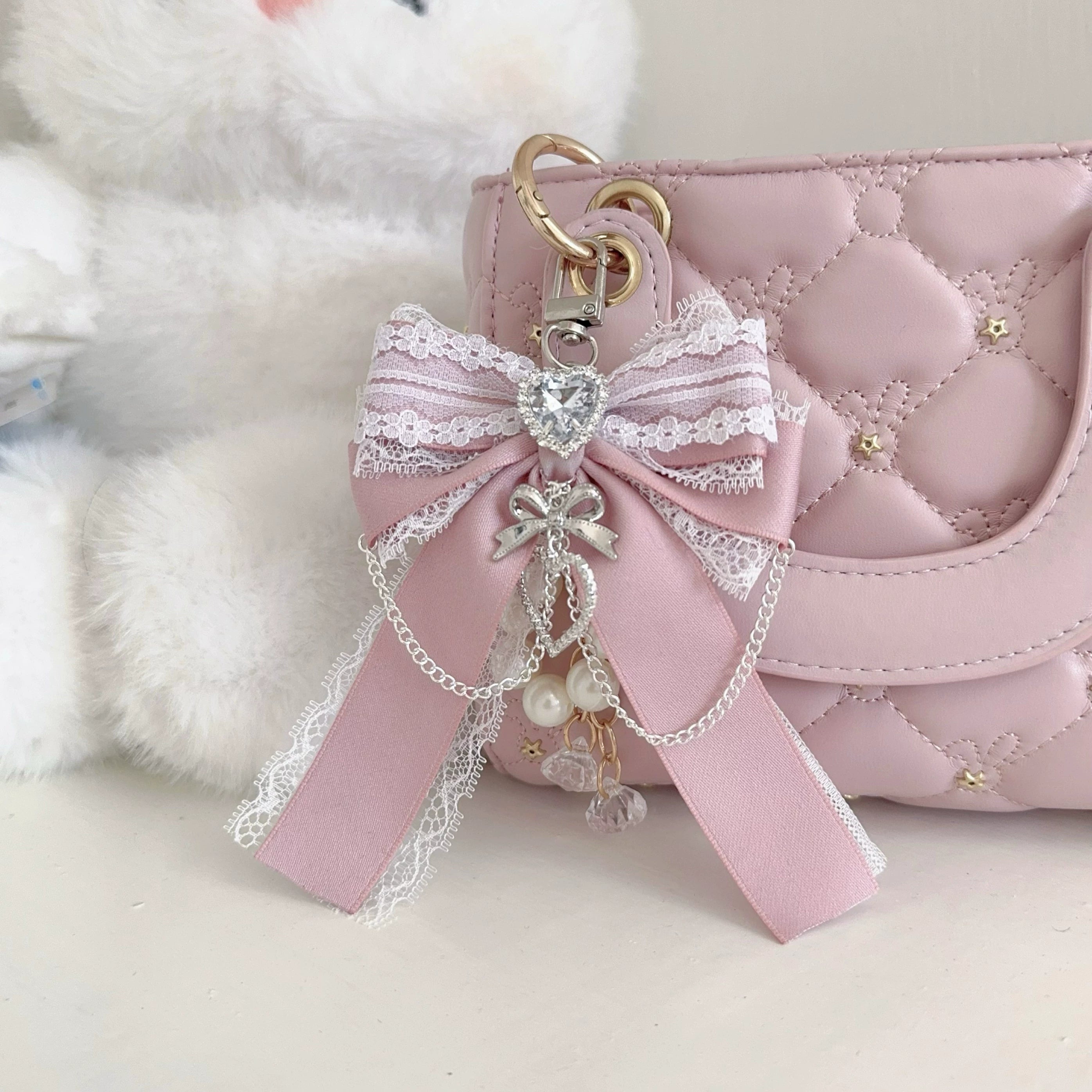 Light lotus pink Ryousangata bow bag pendant with heart rhinestone on quilted handbag - close-up eye-level view of delicate lace bow and pearl tassel charm