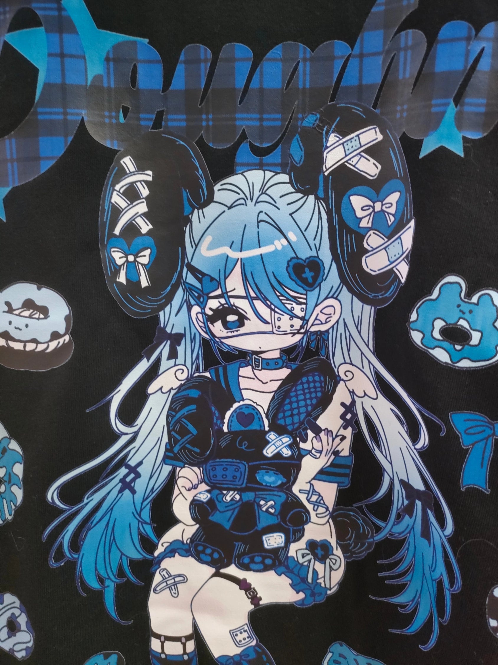 Flat lay front view of blue and black Jirai Kei anime T-shirt print design showing masked anime girl with band-aids, blue plaid lettering, and decorative donut bow star motifs