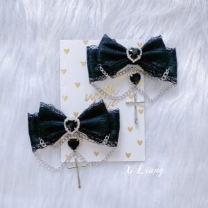 Jirai kei hair accessory featuring black lace bow with heart rhinestones and metal chain embellishments shown on decorative heart-patterned display surface