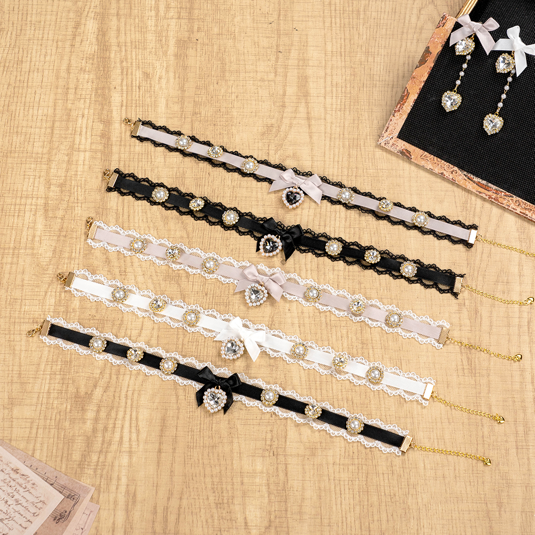 Assorted Jirai Kei choker necklaces with bow and rhinestone embellishments in multiple color variations displayed on wooden table with paper note