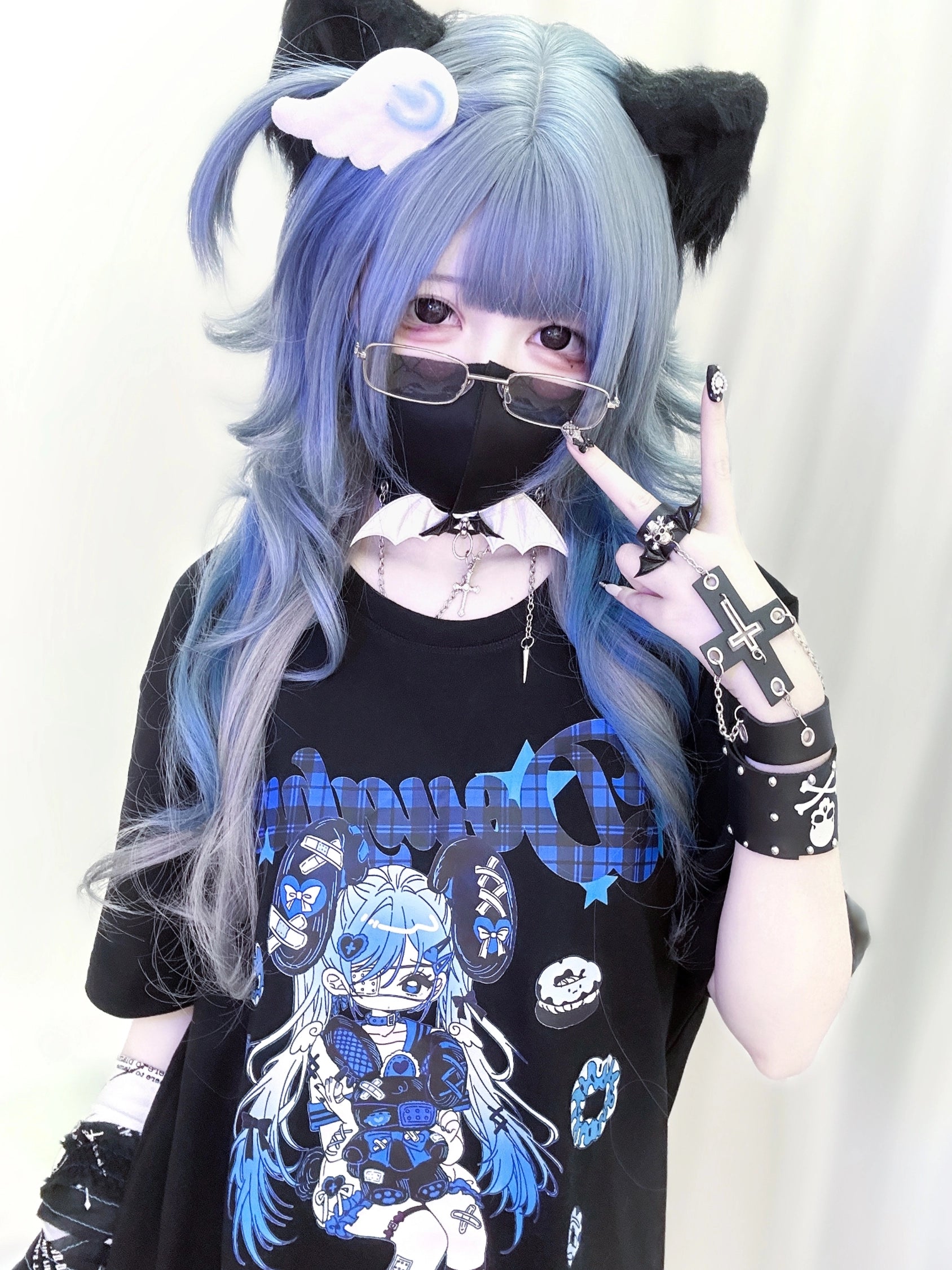 Close-up front mirror selfie of Jirai Kei anime punk T-shirt showing blue anime girl print design, model wearing multiple punk rings, black frame glasses, and band-aid themed accessories