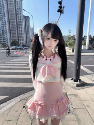 Jirai Kei sailor collar two-piece set with detachable bunny ear blouse and removable polka-dot bow, worn by twin-tailed model on urban crosswalk, pink and off-white kawaii lolita aesthetic