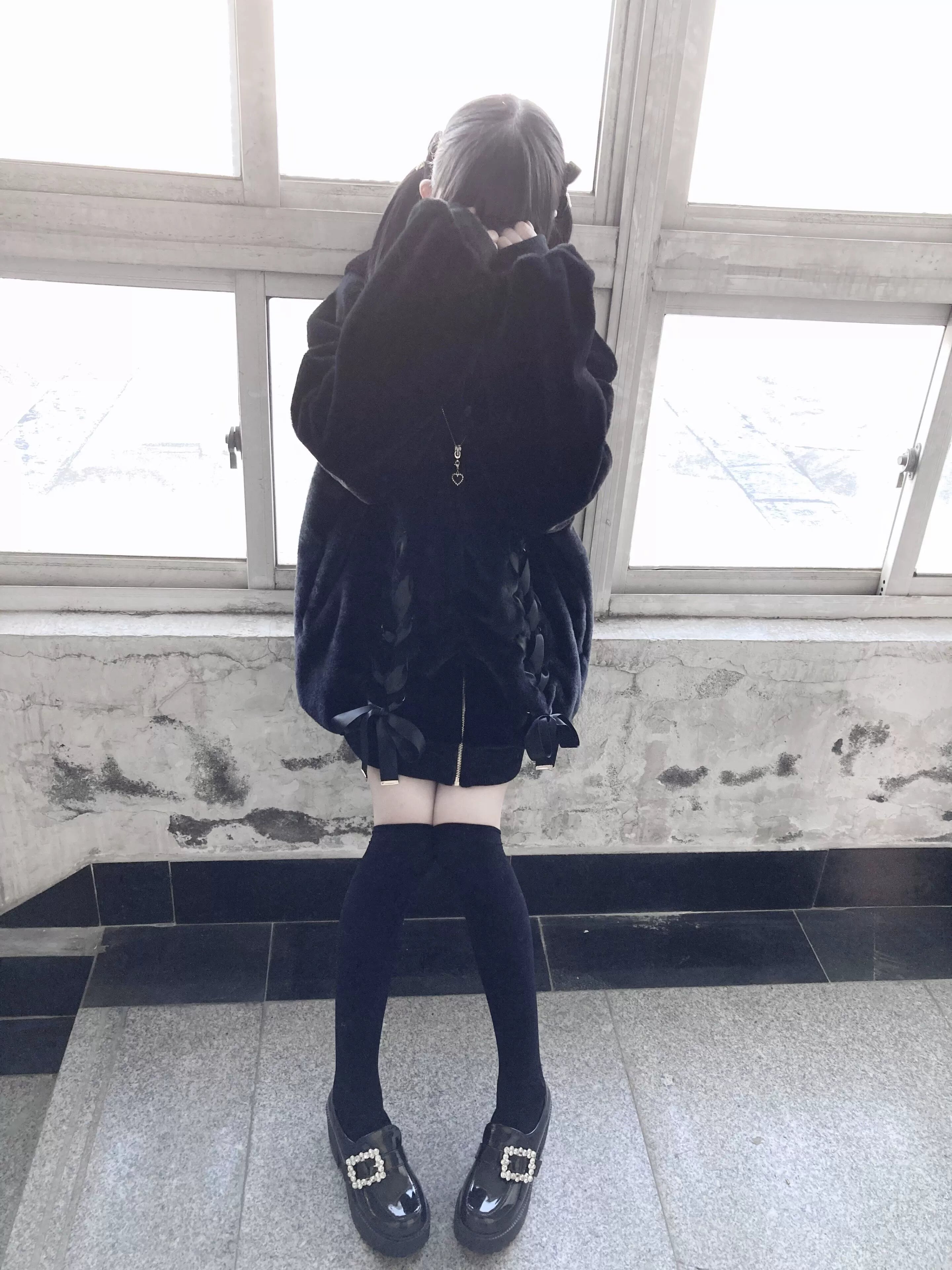 Black plush fleece coat back view showing oversized silhouette and hem detail on model with school uniform aesthetic