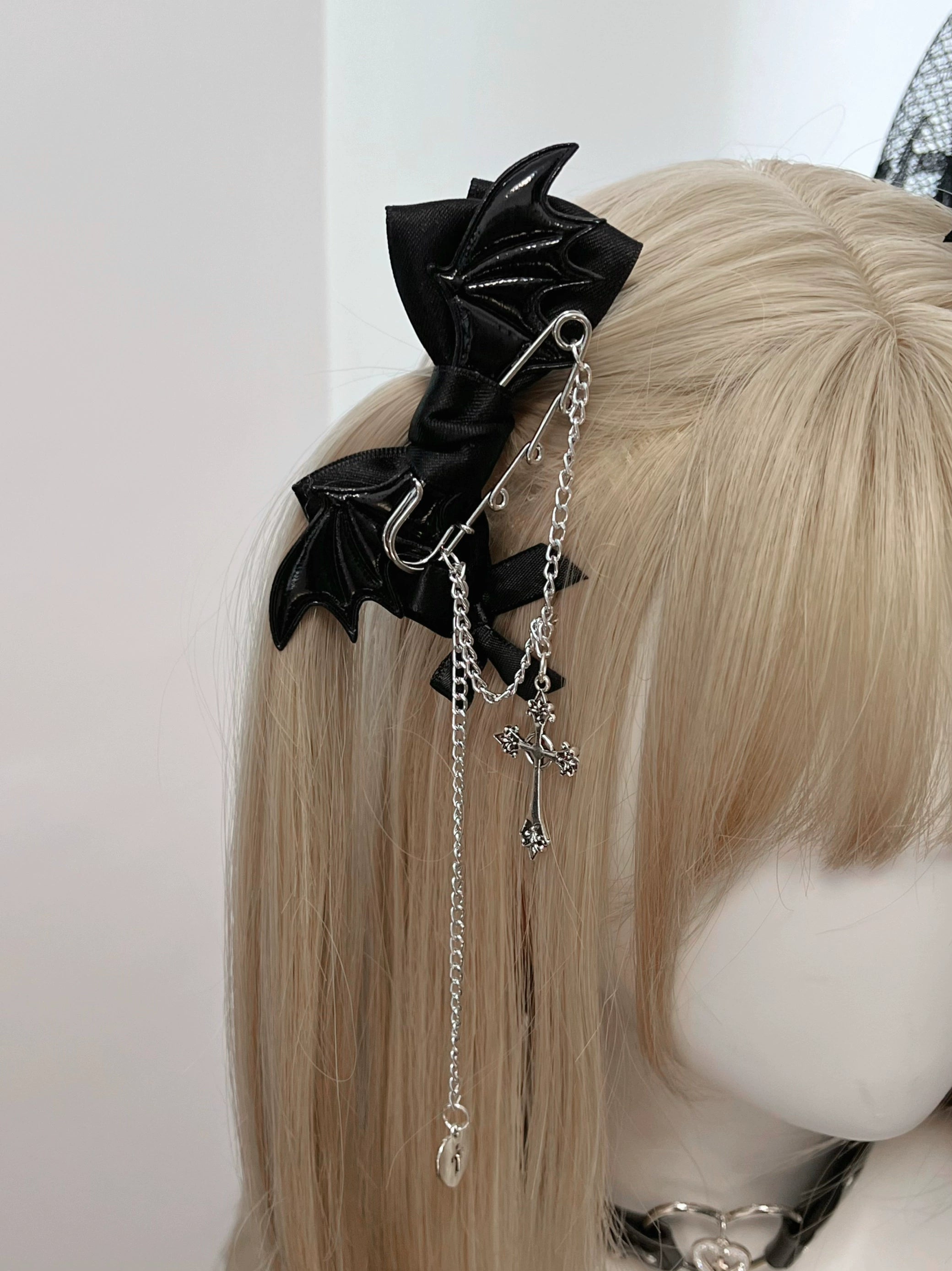 Close-up front view of black winged bat bow hair clip showing long silver chain with cross pendant - detailed Jirai Kei hair accessory close-up shot