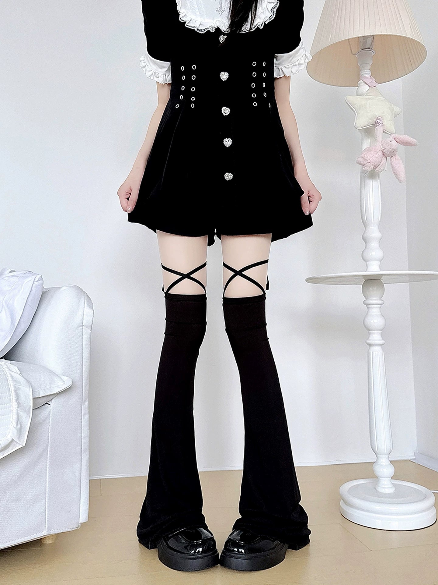 Black jirai kei over-the-knee leg warmers with prominent cross-strap design, flared hem silhouette, worn with black lolita mini dress, detailed strap configuration view