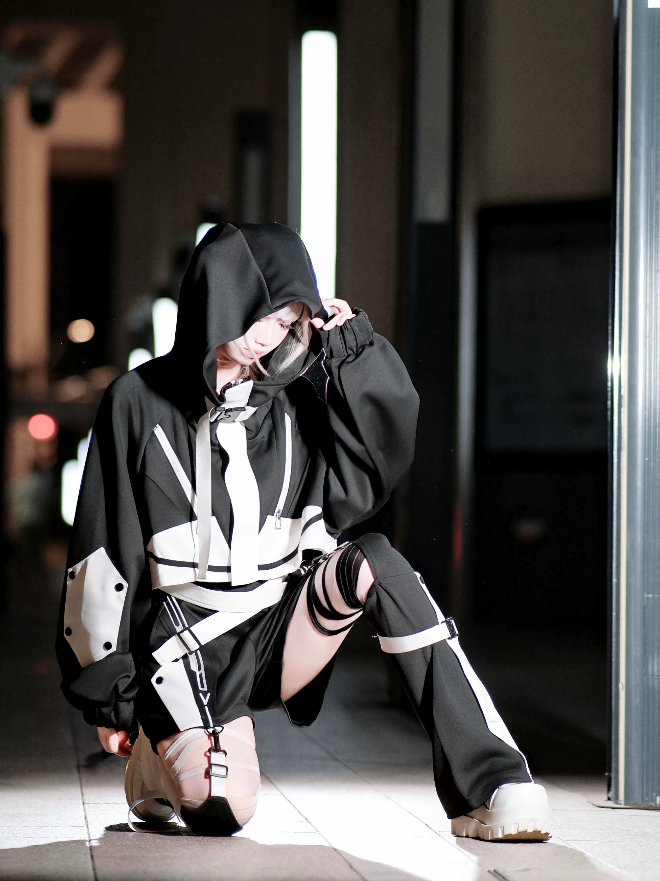 Black white oversized cyberpunk jirai kei hoodie set with ripped thigh covers color block silhouette on kneeling model night scene