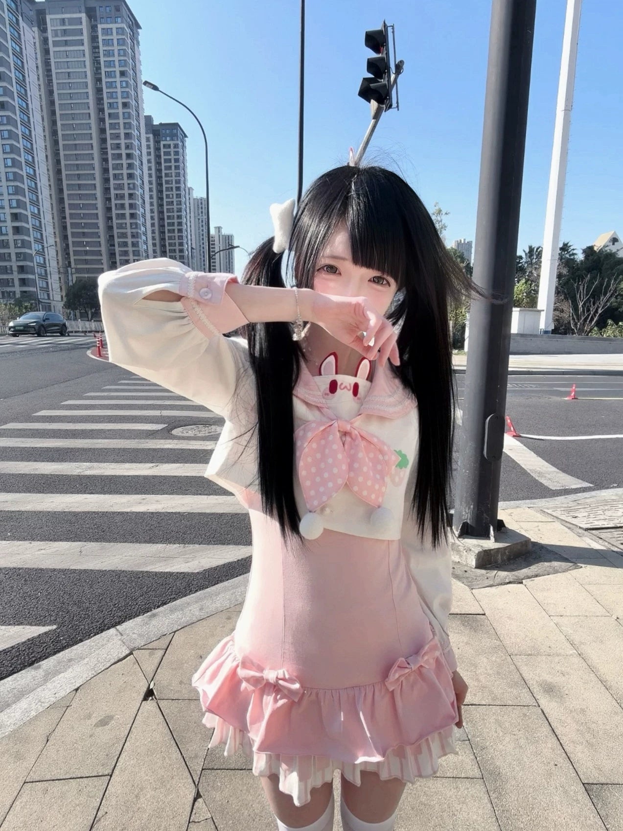 Front eye-level view of long-sleeve sailor collar Jirai Kei two-piece set with rabbit decor, removable polka-dot bow, ruffle mini skirt, twin-tailed model on urban crosswalk