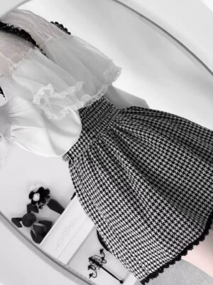 Overhead flat lay display of sheer lace blouse and houndstooth pleated suspender skirt