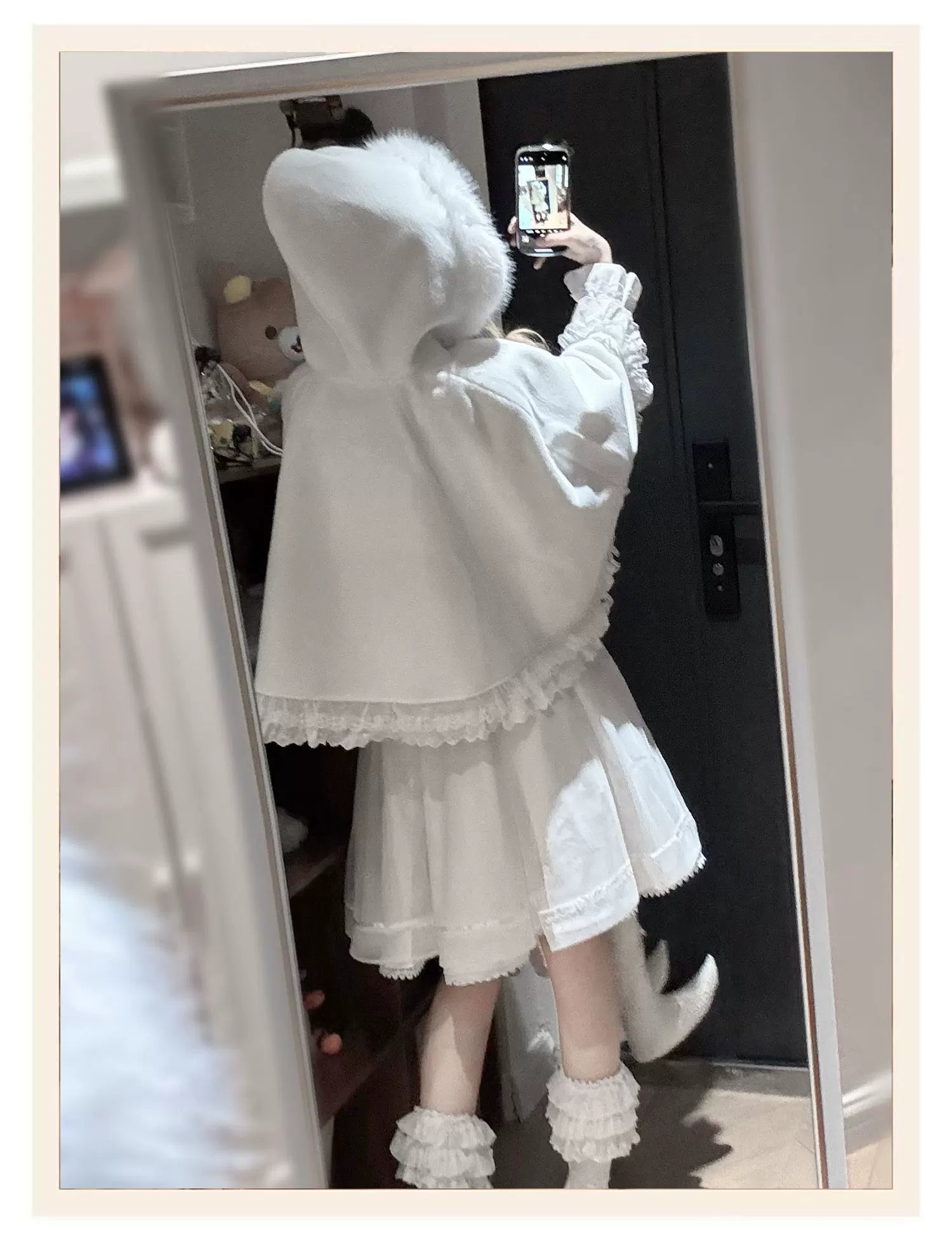 White hooded cape with faux fur collar and scalloped lace hem worn with ruffled high-waist skirt, back mirror view