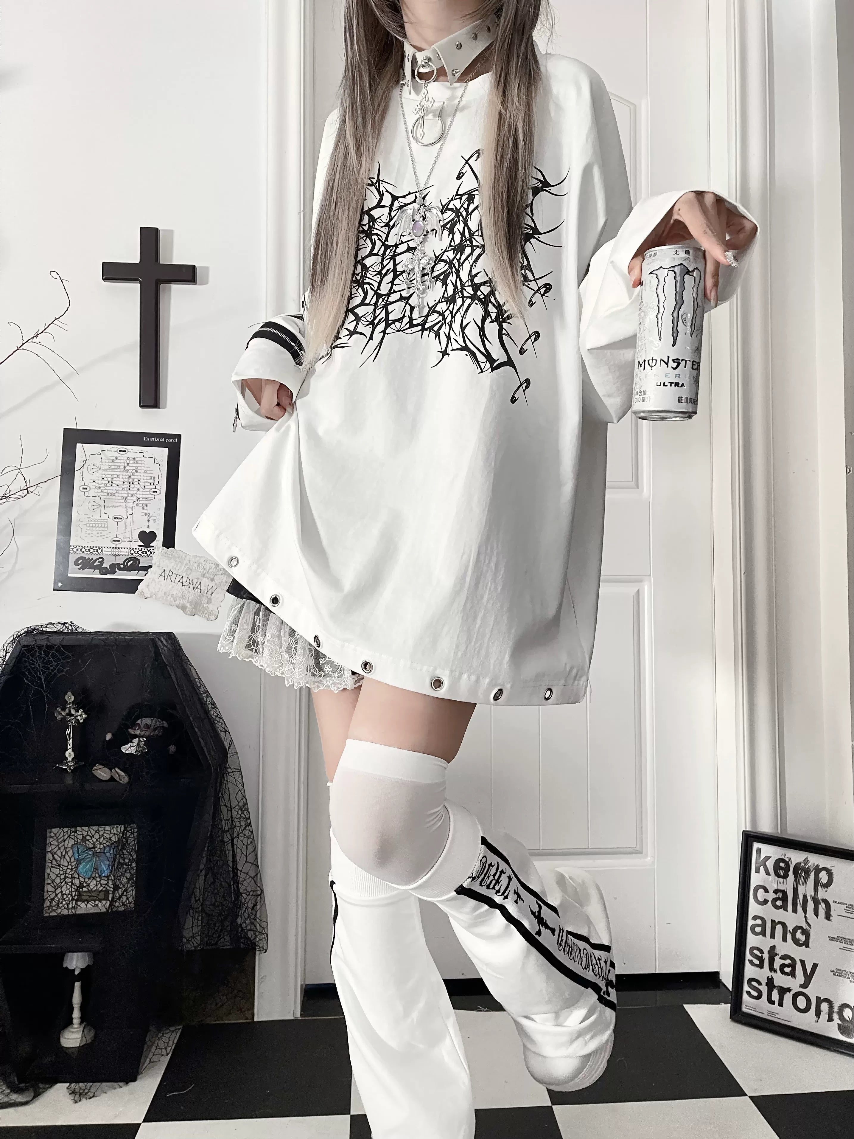 White jirai kei oversized gothic long-sleeve tee with black thorn cross print, riveted lace hem, and cross strap sleeve details, worn with thigh-high socks in alternative fashion setting