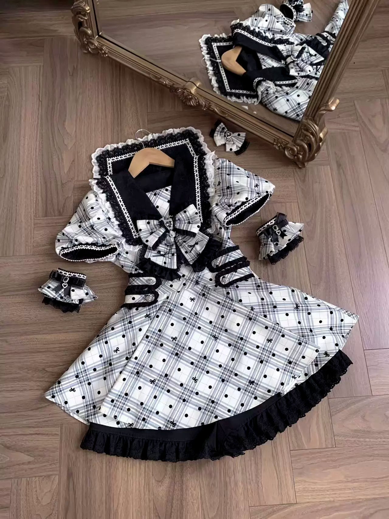 Top-down flat lay of complete Jirai Kei dress set on wooden floor background including sailor collar dress, matching decorative wrist cuffs, and black lace trim details with mirror