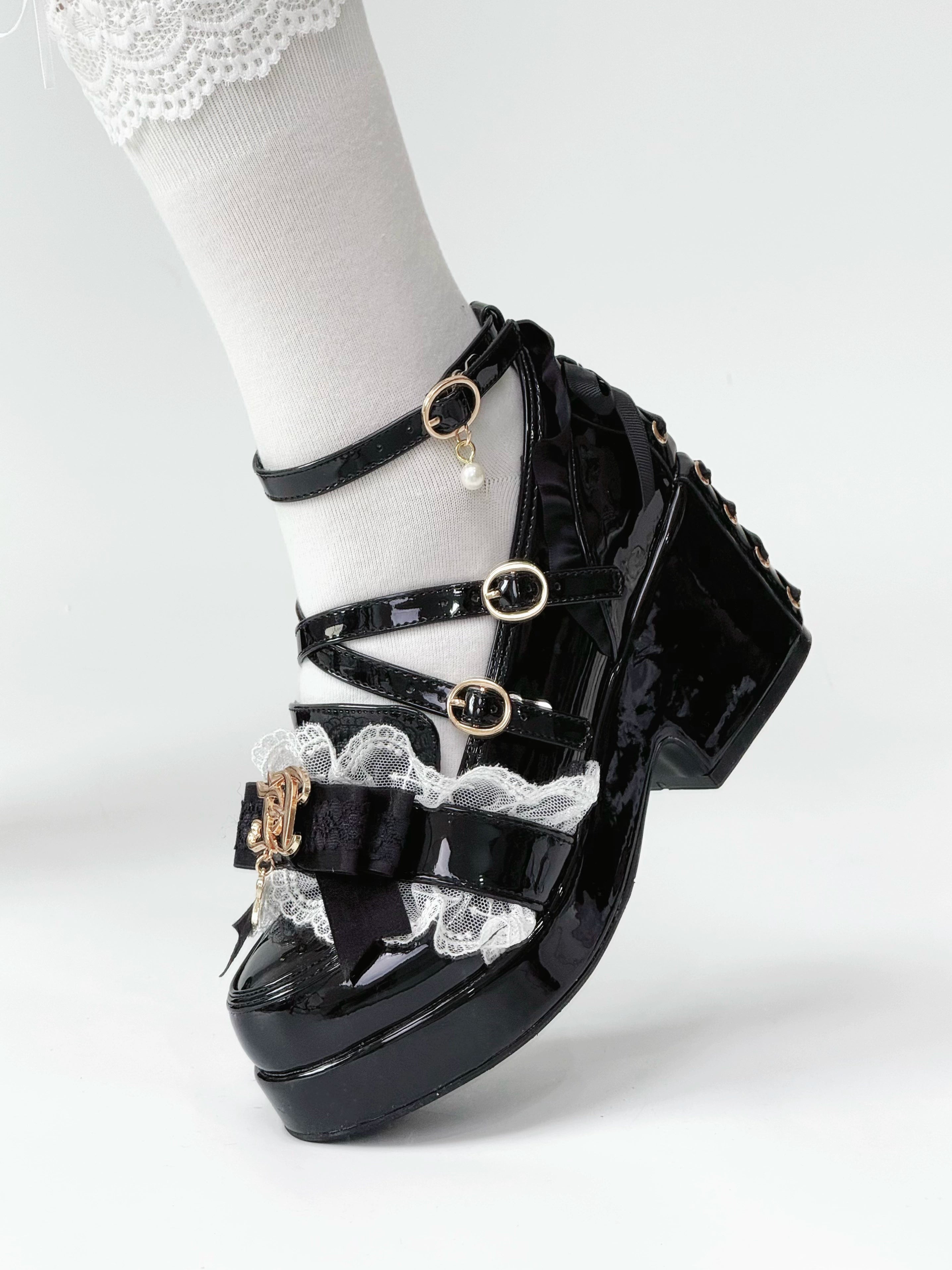 Single black patent leather Jirai Kei platform heel side profile view with white ruffled sock displaying crisscross buckle straps lace trim and high block platform construction