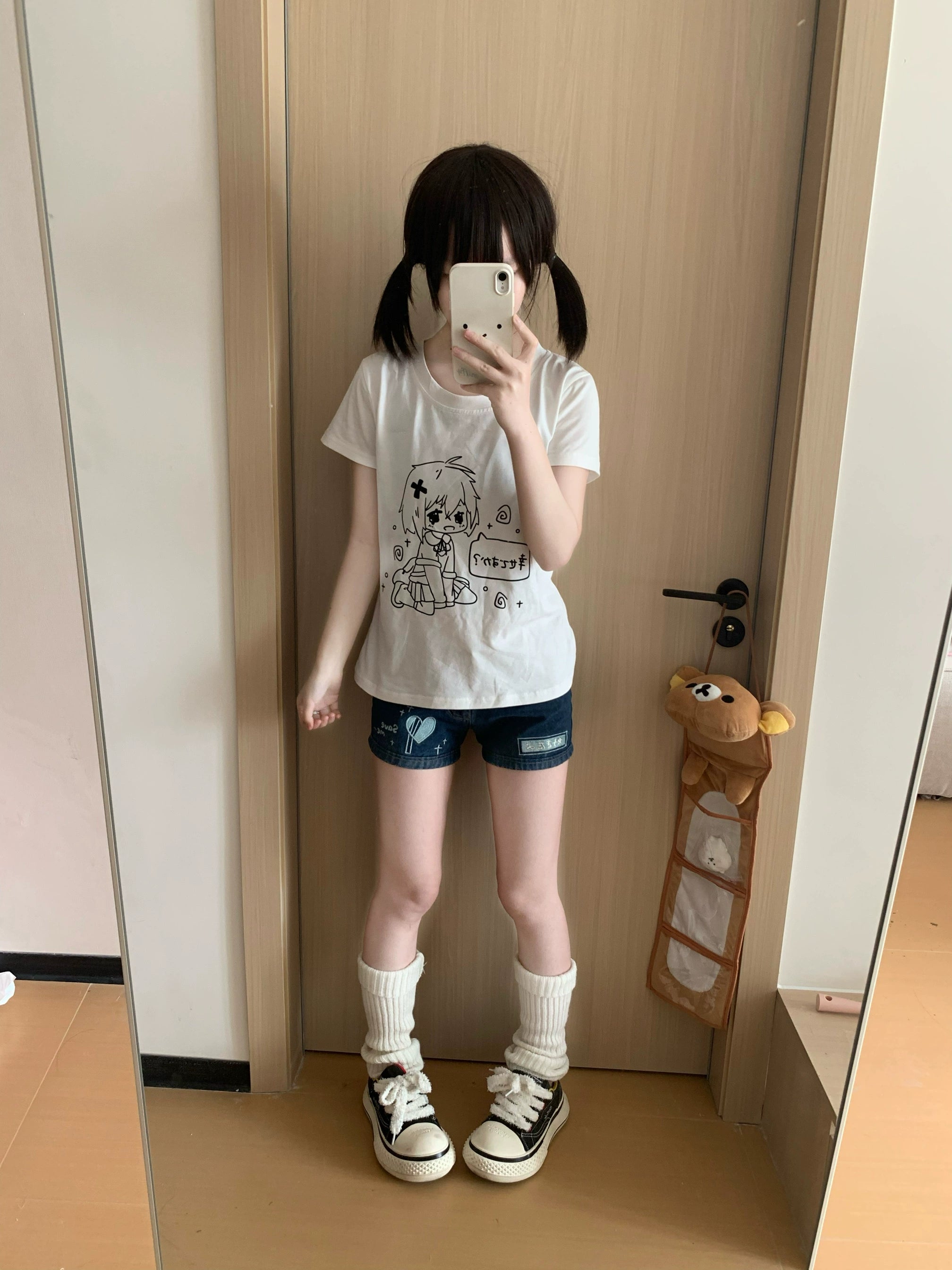 Jirai Kei white anime graphic t-shirt front view on model wearing twin-tails hairstyle in home doorway mirror selfie