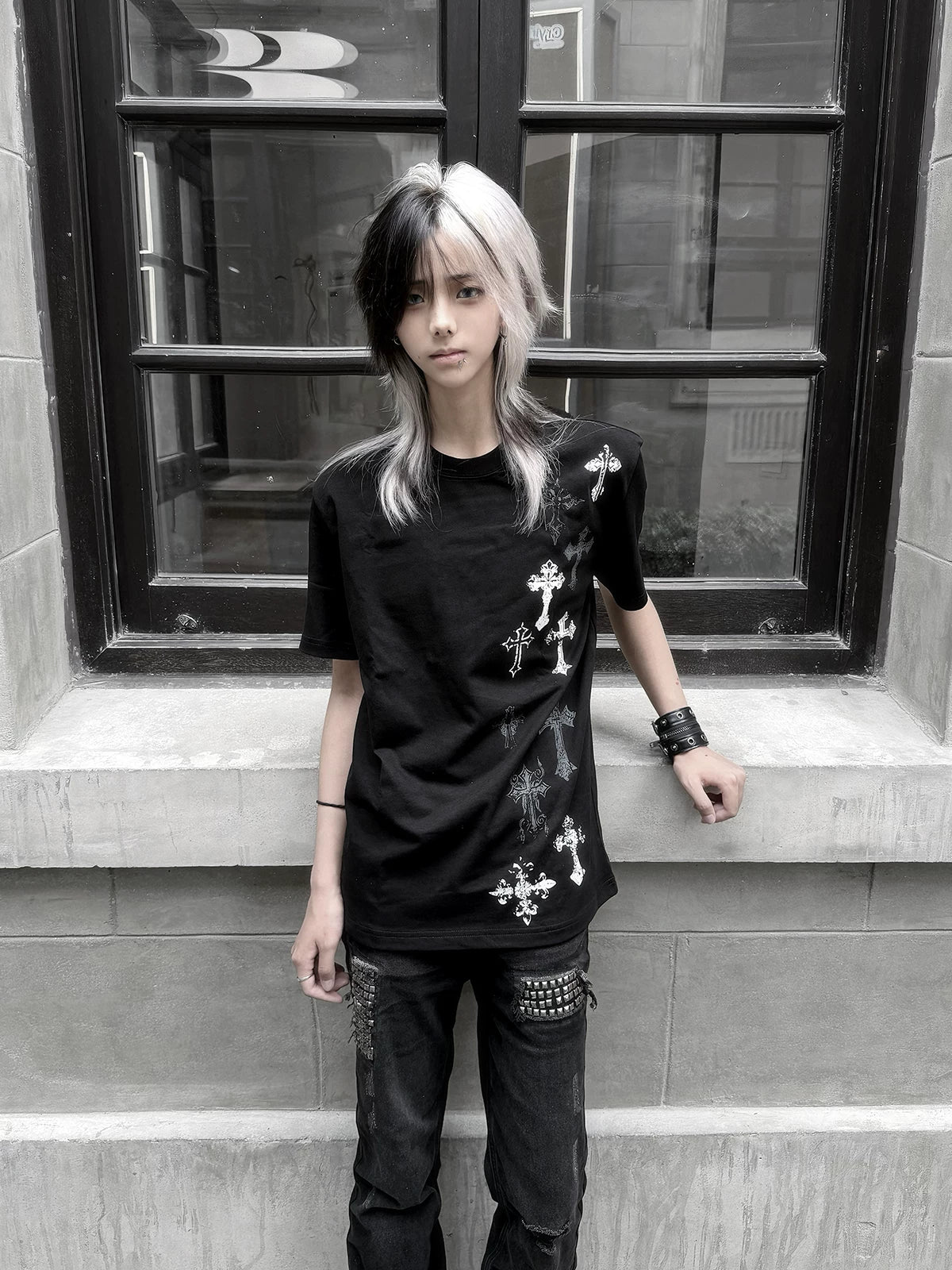Black cross print t-shirt front full body view on female model, silver cross prints visible on left chest and lower garment, outdoor window background