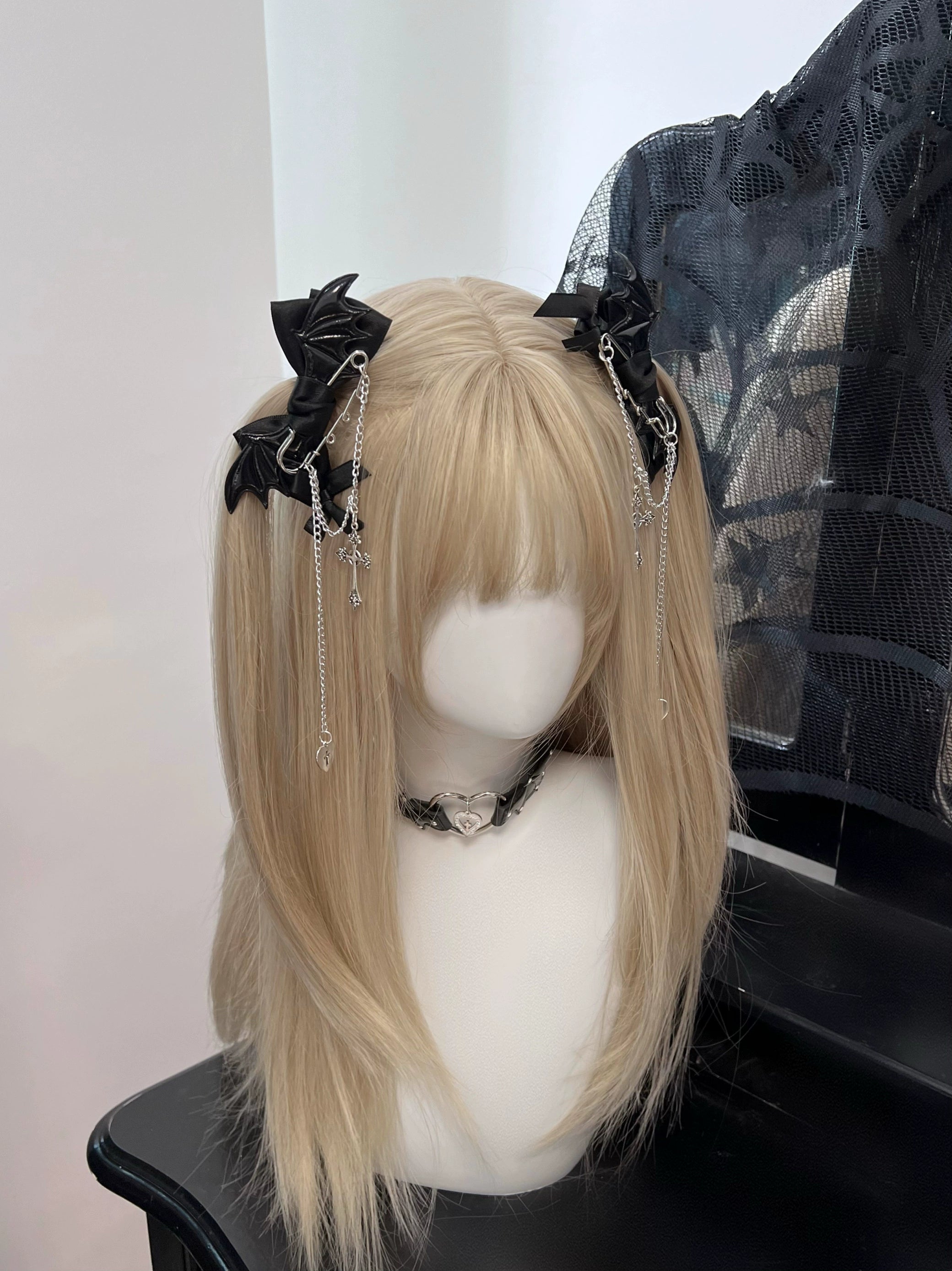Pair of black winged bat bow hair clips with hanging silver chains on blonde shoulder-length wig mannequin - back three-quarter view showing Jirai Kei dual clips styling
