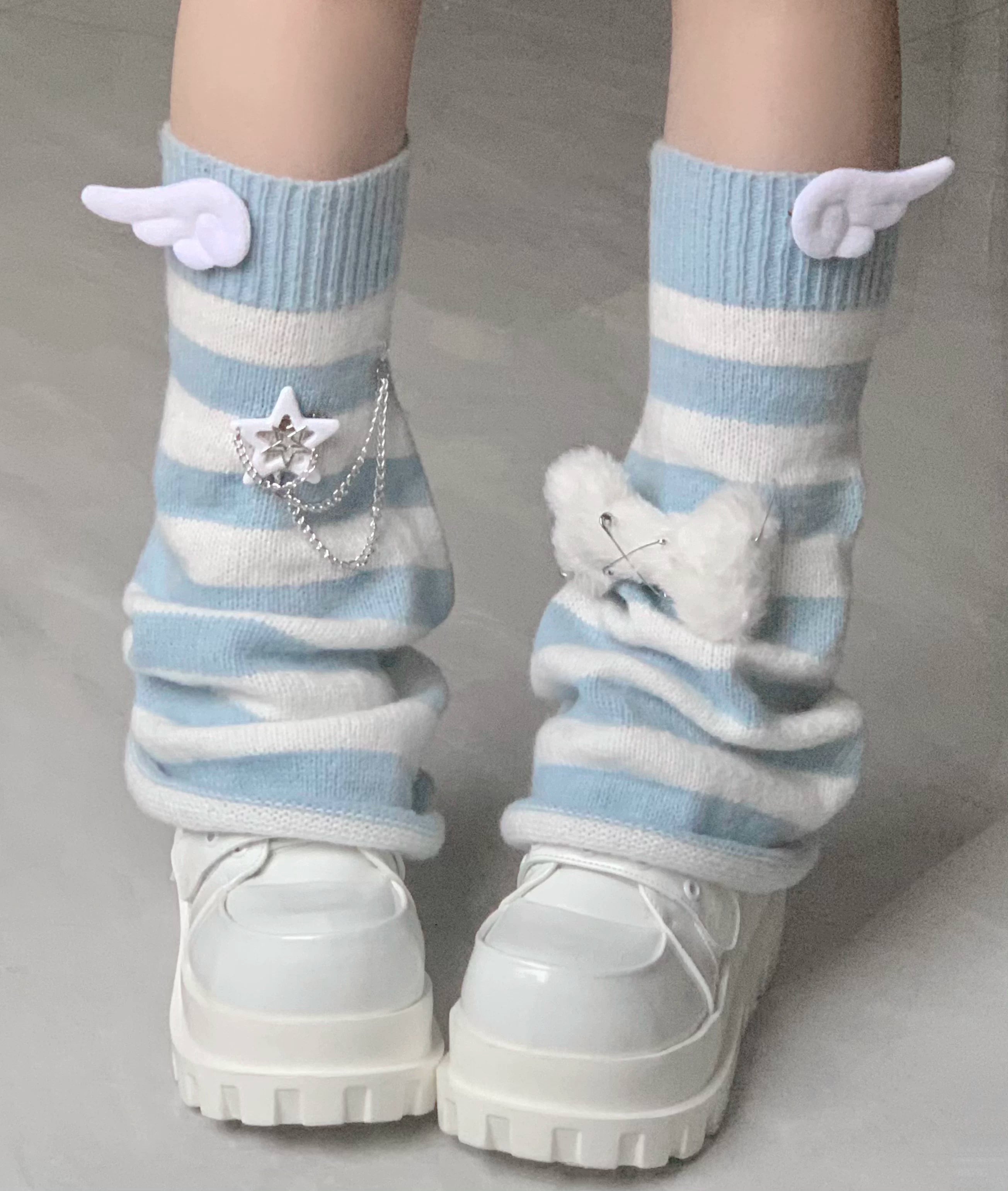 Calf close-up of light blue and white striped leg warmers with angel wing fluffy bow and star chain decorations and white platform loafers